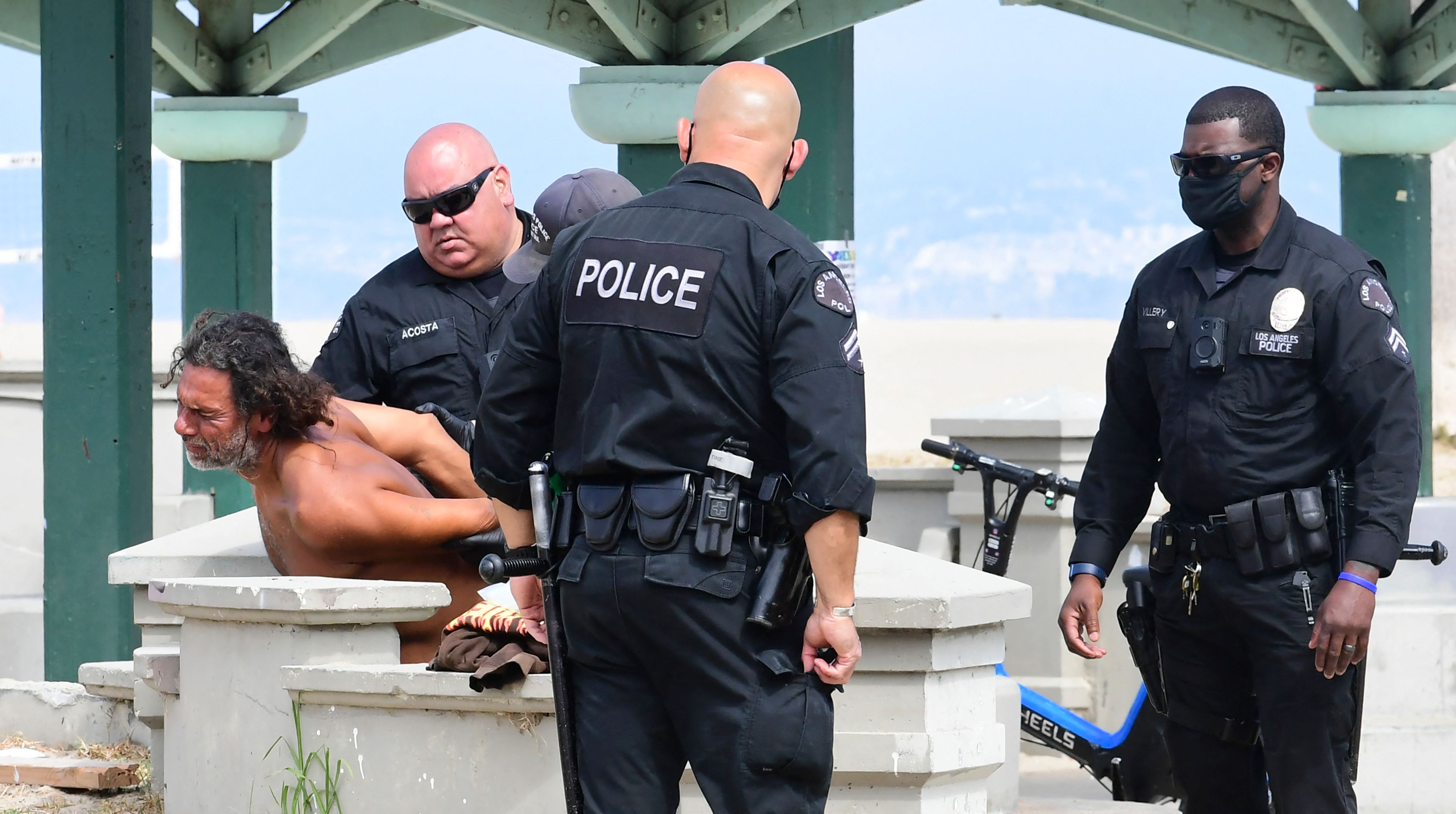 A Los Angeles police officer in Oakley sunglasses looks on during a homeless sweep on Venice Beach in 2021