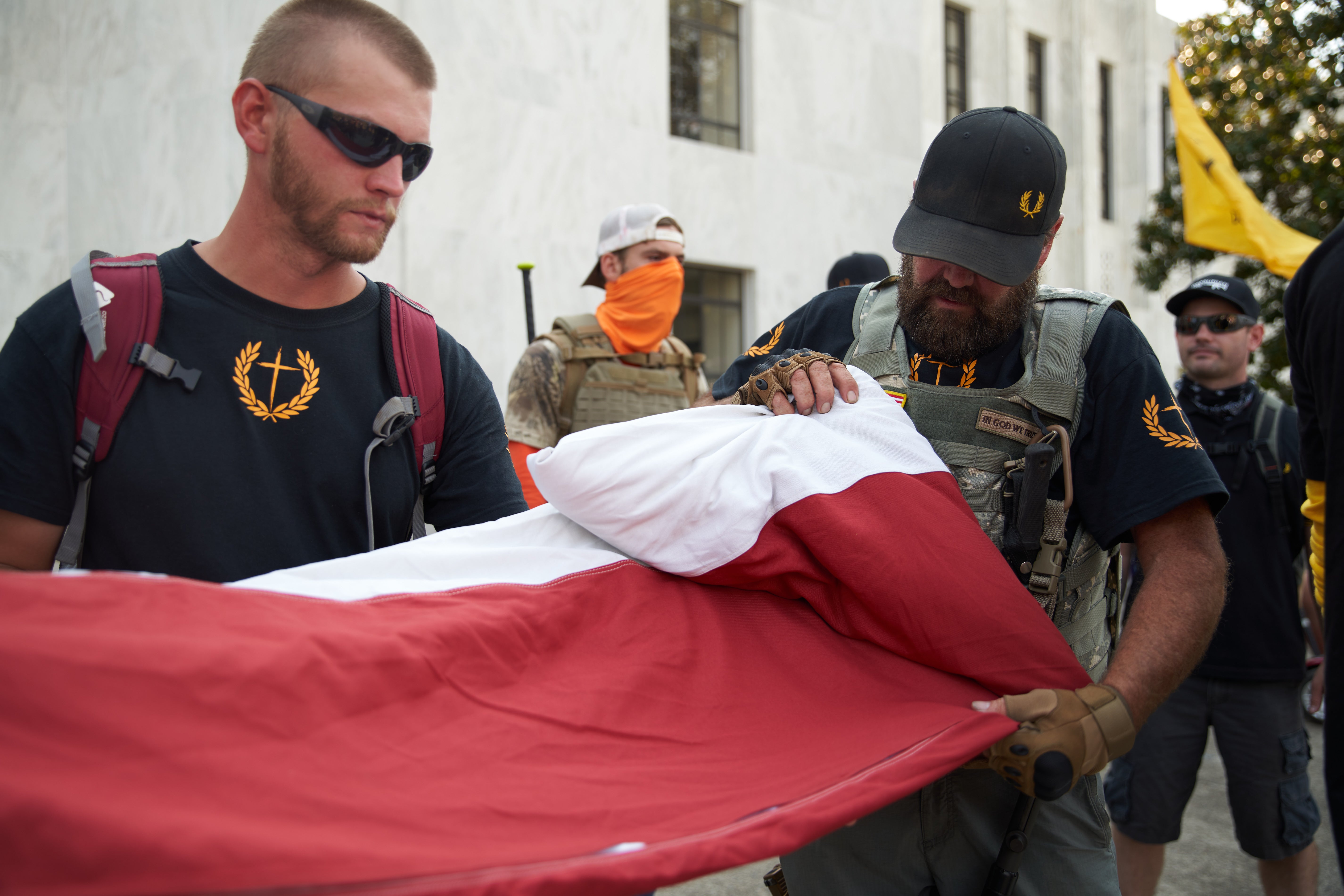 A member of the Proud Boys wearing Oakley glasses helps roll up a US flag as Trump supporters and members of the alt-right conservative groups Patriot Prayer and Proud Boys converge in Salem, Oregon on September 7, 2020