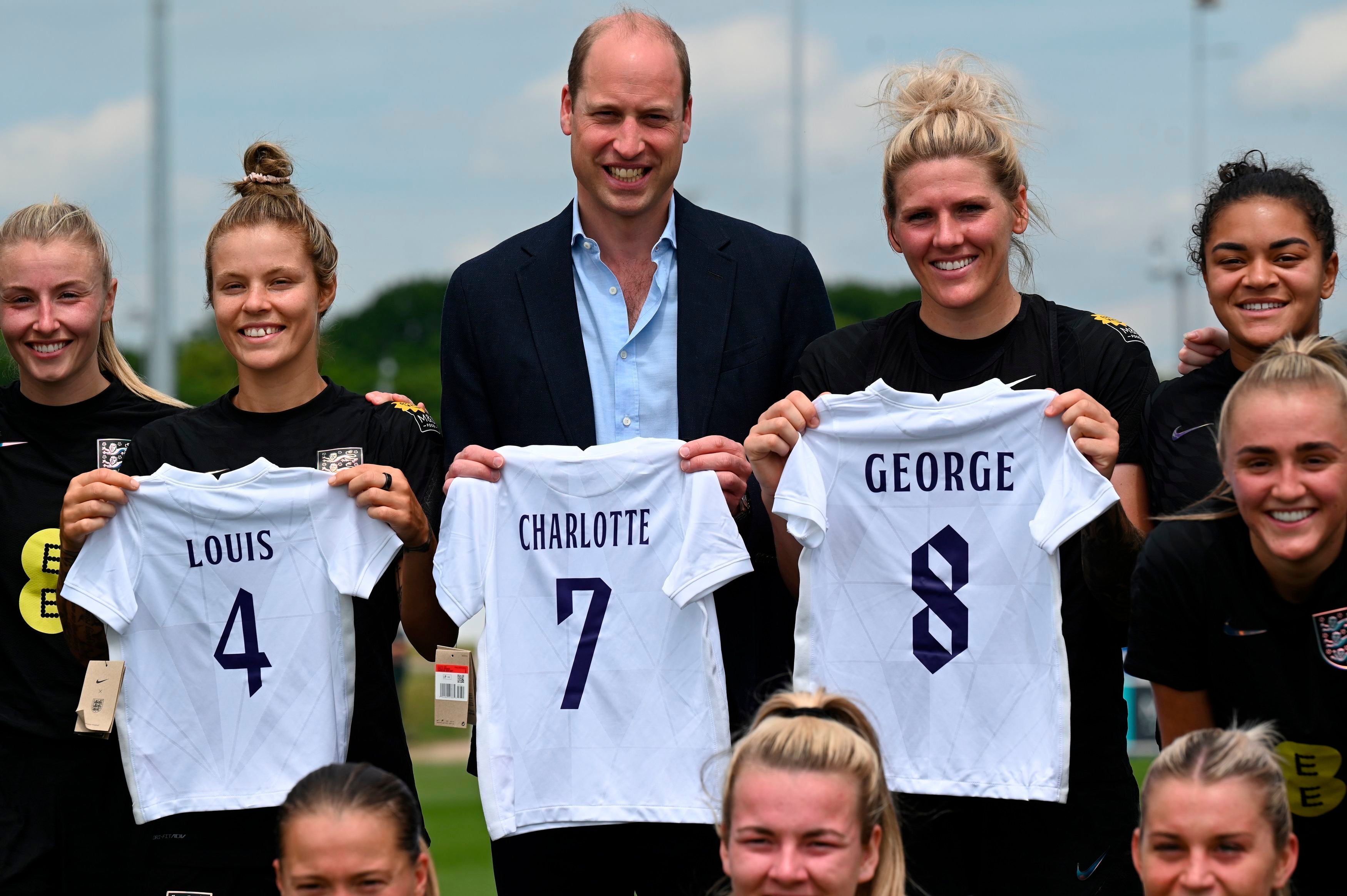 Prince William holding the England football jersey bearing the names of his three children and with the England women football team