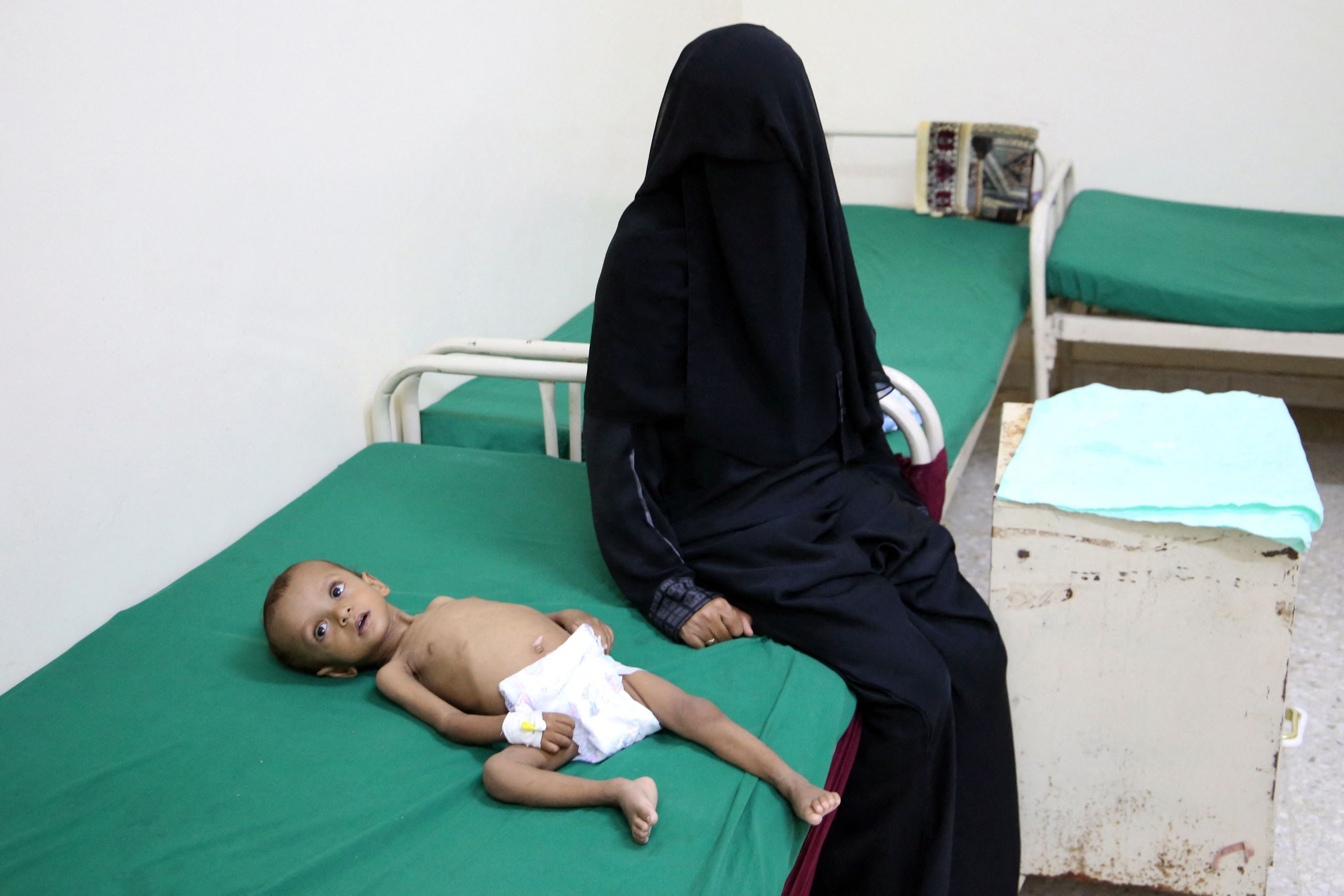 A woman sits next to a malnourished child, lying on a bed at a treatment centre, in the village of Hays in Yemen’s war-ravaged western province of Hodeida