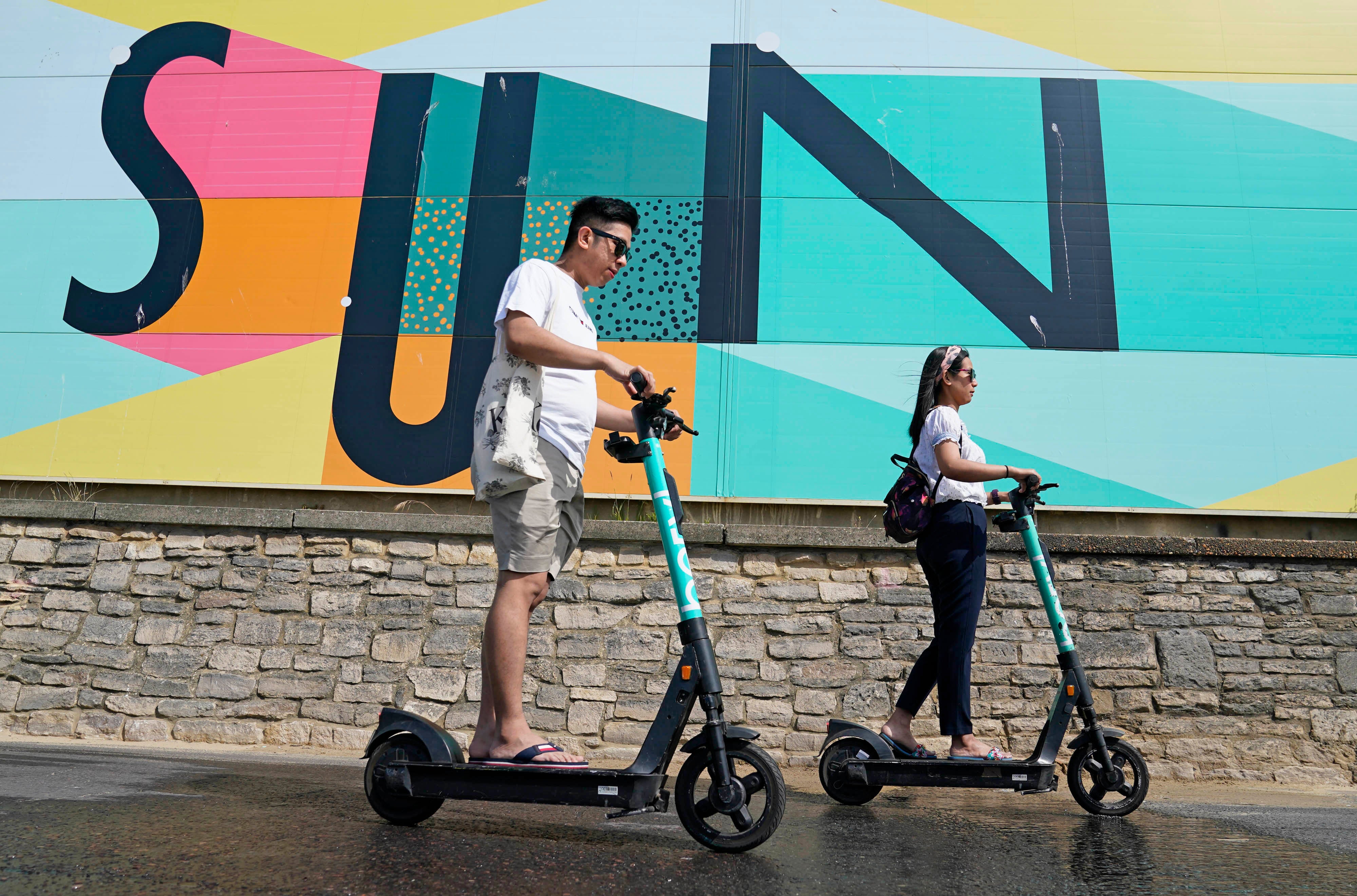 People scooter past a sign at Boscombe Beach in Dorset