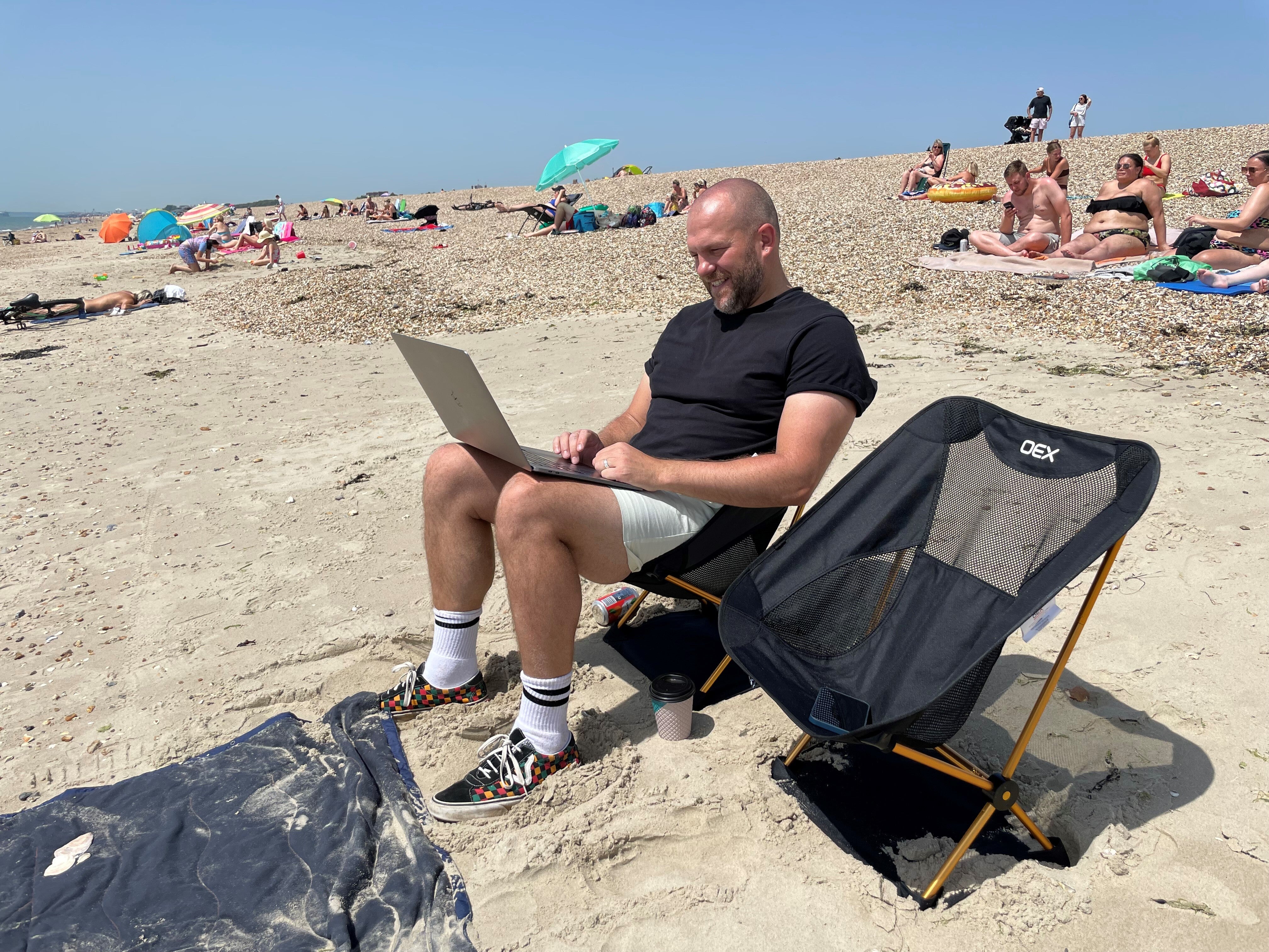 Andrew Clarke, 40, from Basingstoke, a user experience design manager for a mobile phone company checking on his work during his lunch hour on the beach in Southsea, Hampshire