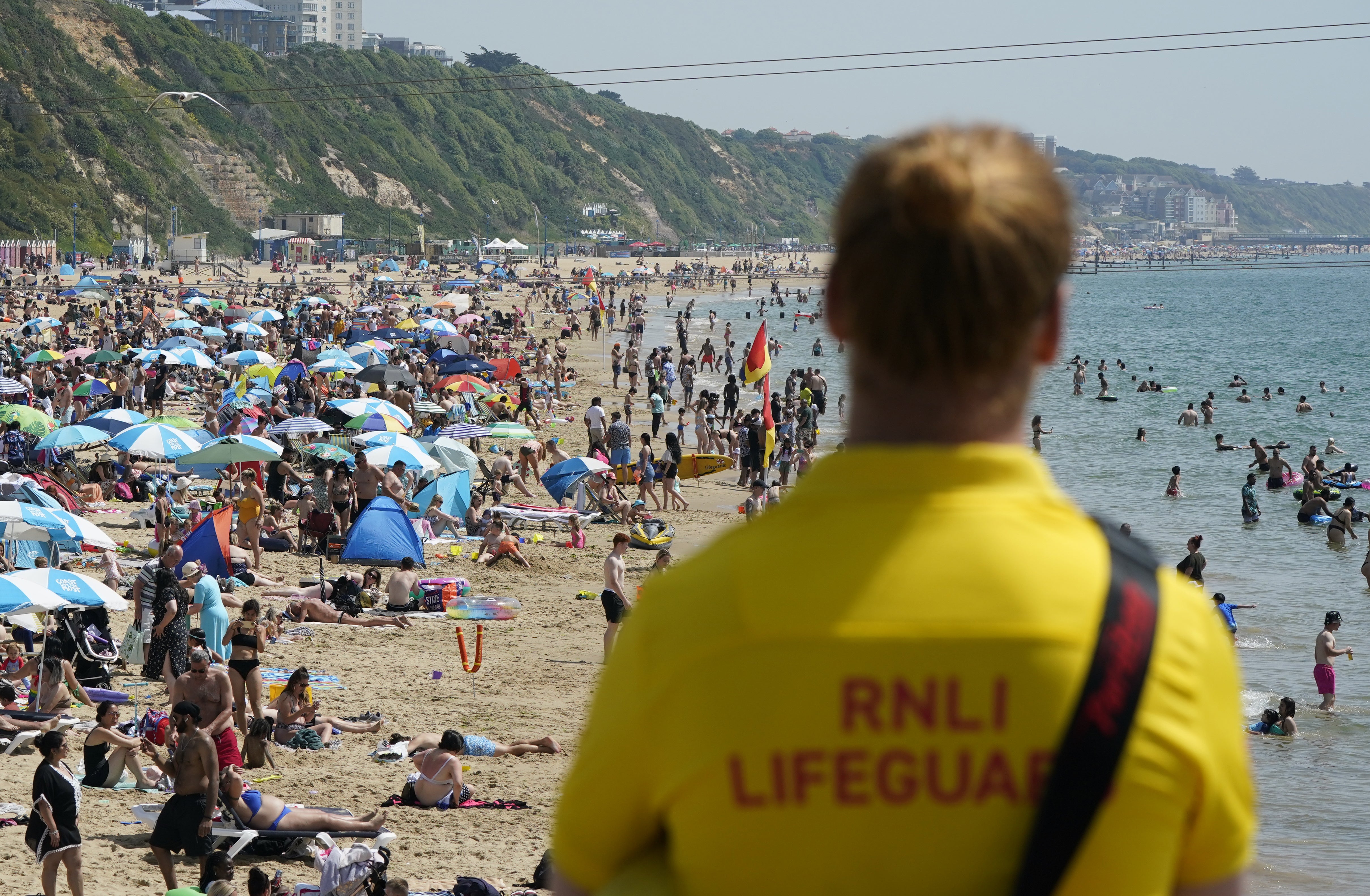 A RNLI Lifeguard looks out from Bournemouth Pier as people enjoy the warm weather on Bournemouth beach in Dorset