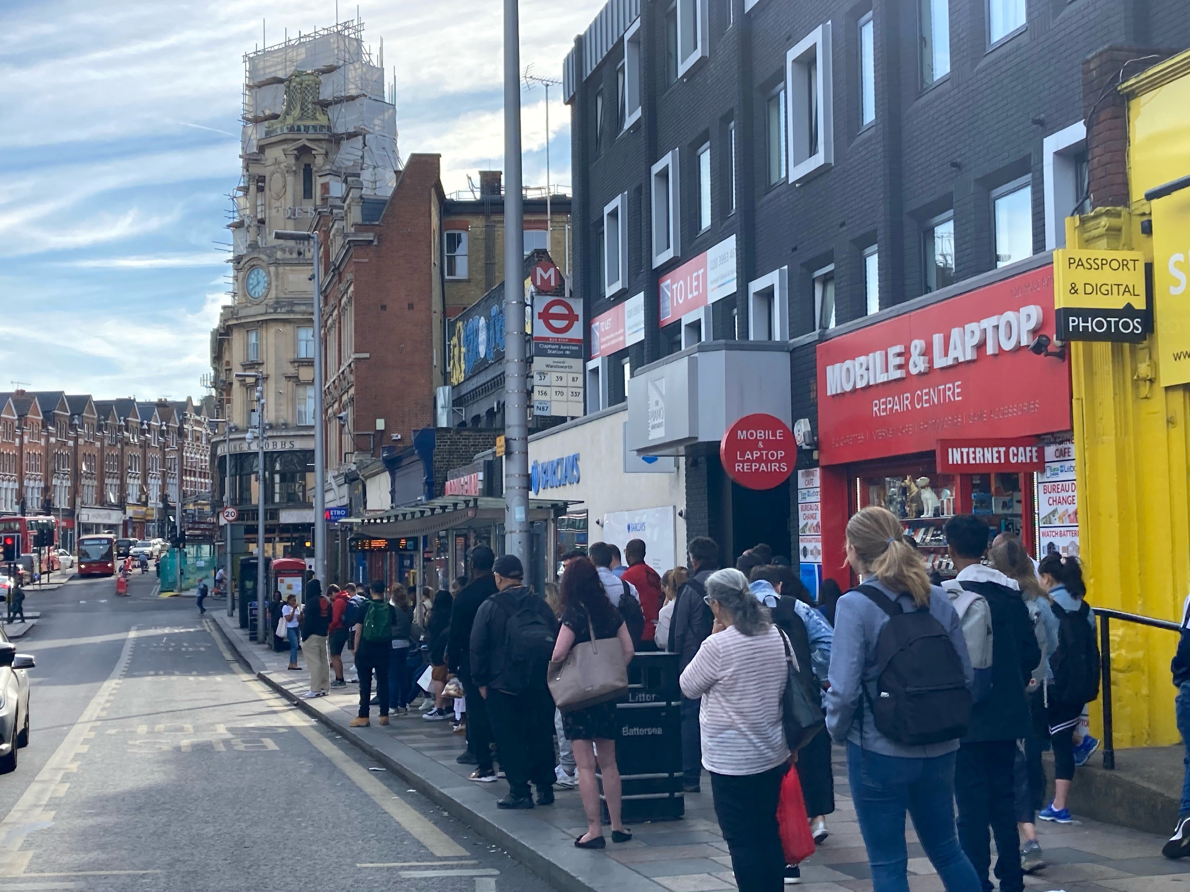 Passengers wait at a bus stop outside Clapham Junction station in southwest London