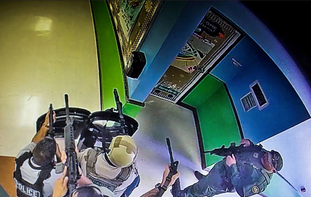 Image, taken from surveillance video in the hallway of Robb Elementary School, shows several officers aiming long rifles towards the two adjoining classrooms