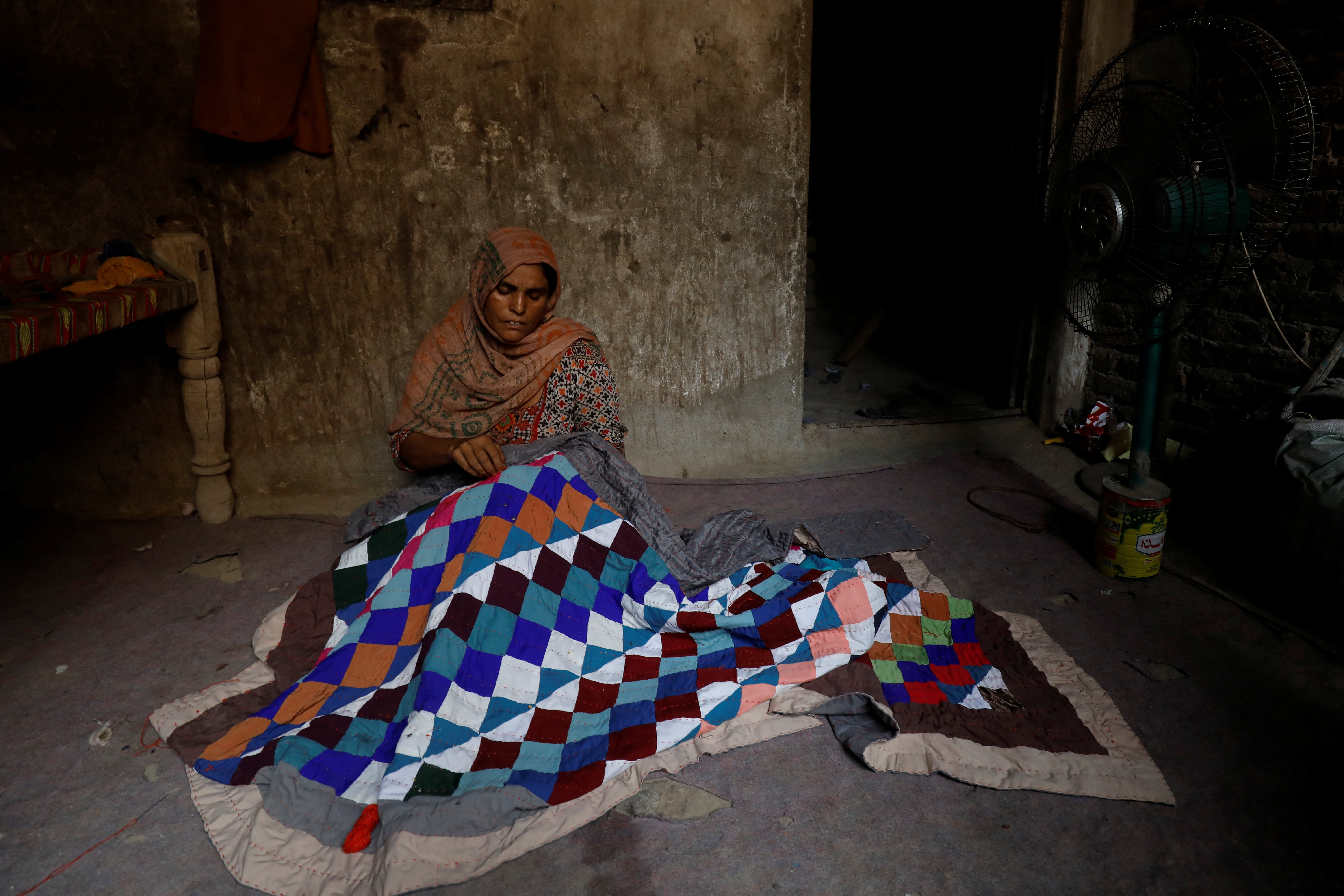 Rehmat stitches a Sindhi ralli quilt while sitting in front of a fan to cool off