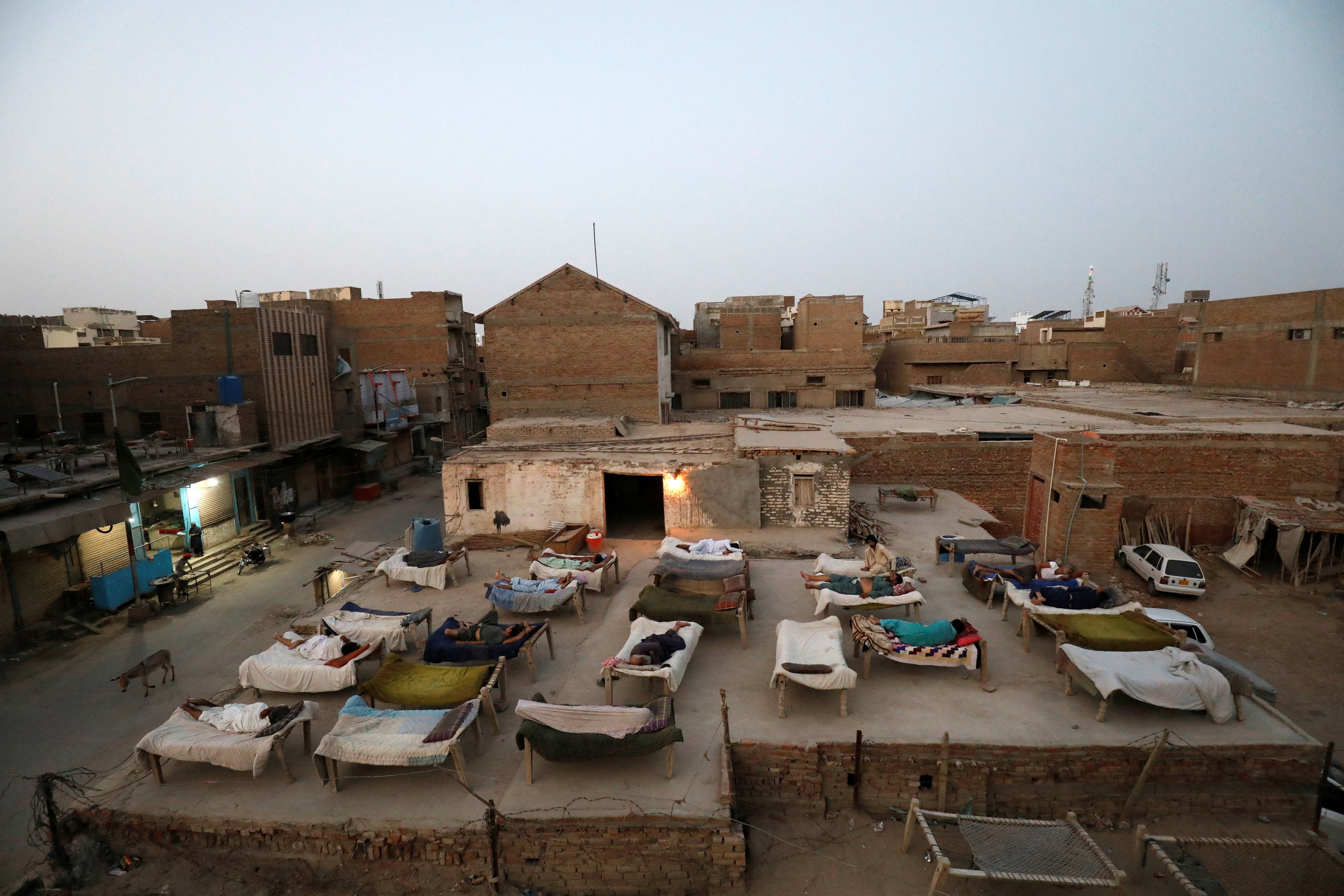 Men sleep on charpoy rope beds on a roof early in the morning during a heatwave