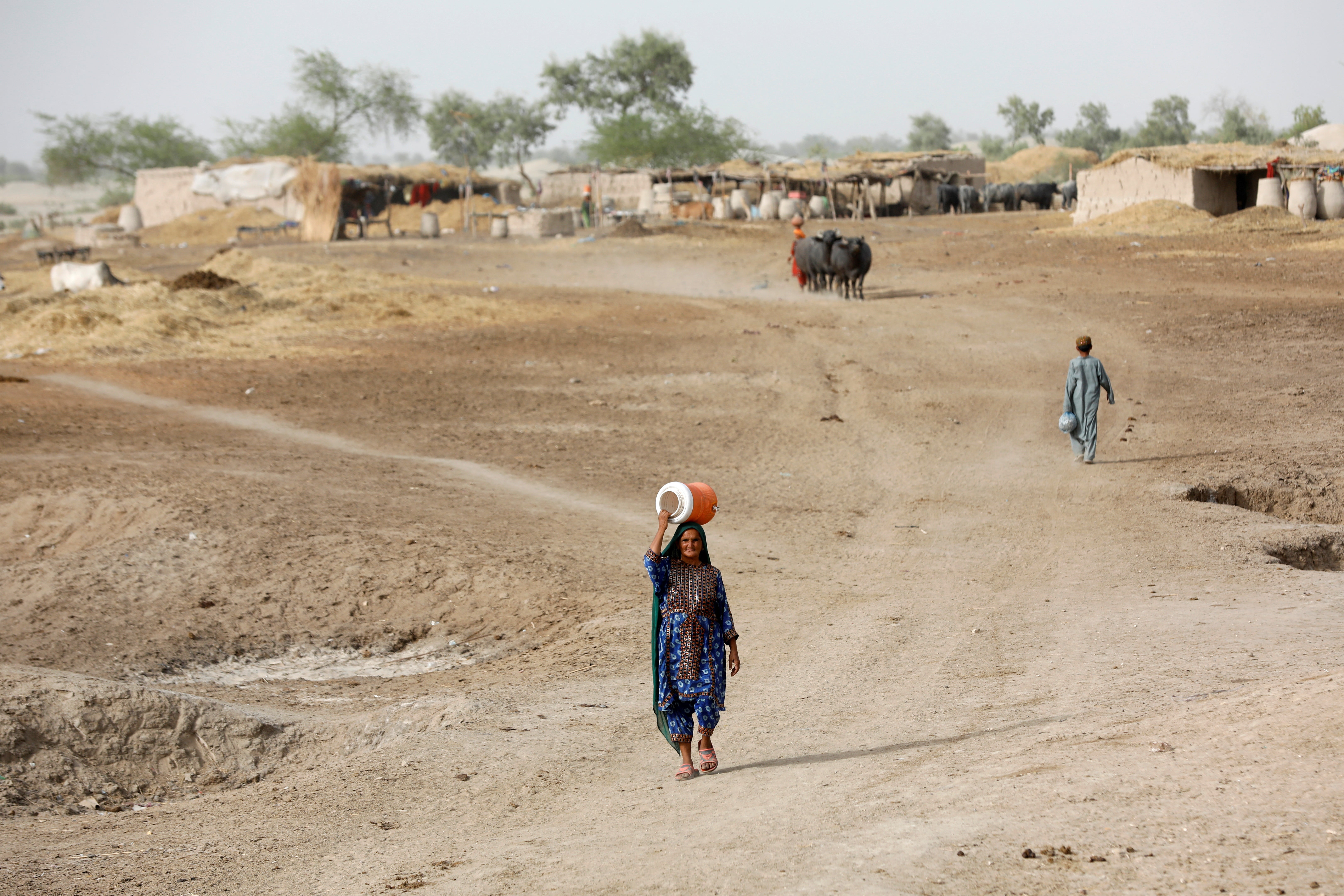 A woman walks to fetch water from a nearby hand-pump with a water cooler on her head