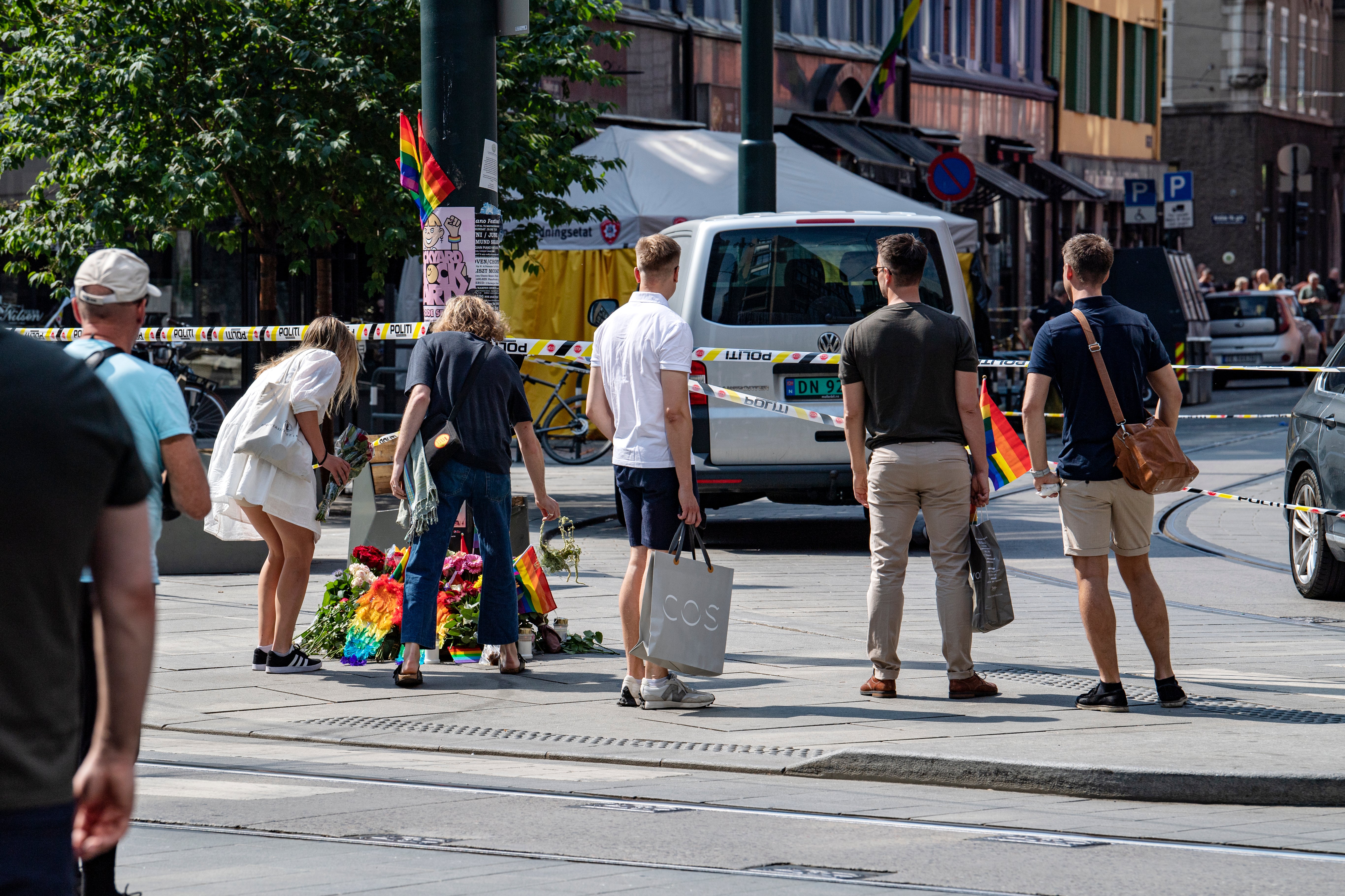 People lay rainbow flags along the street near a restaurant with windows shattered by the shooting