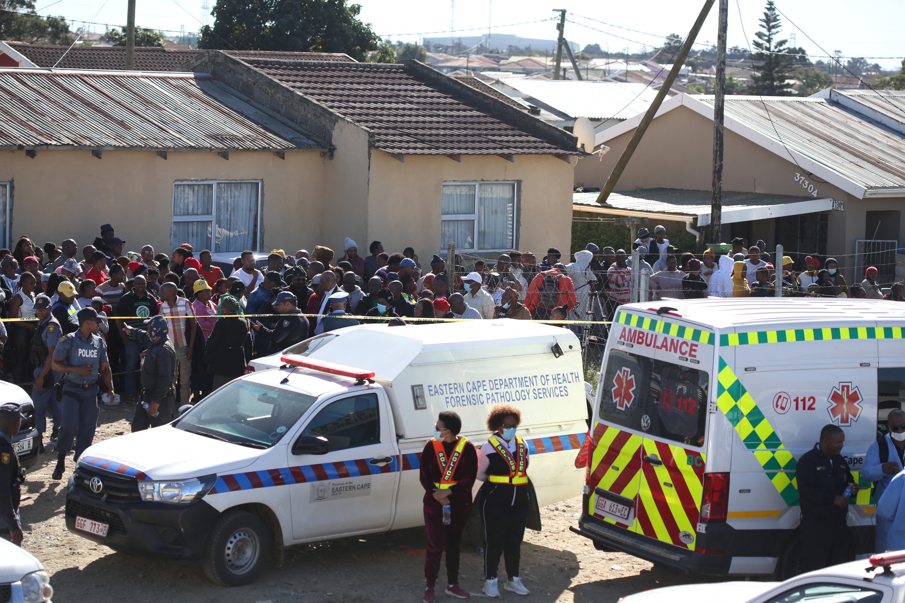 A crowd gathers as forensic personnel investigate after the deaths of patrons of the Enyobeni Tavern