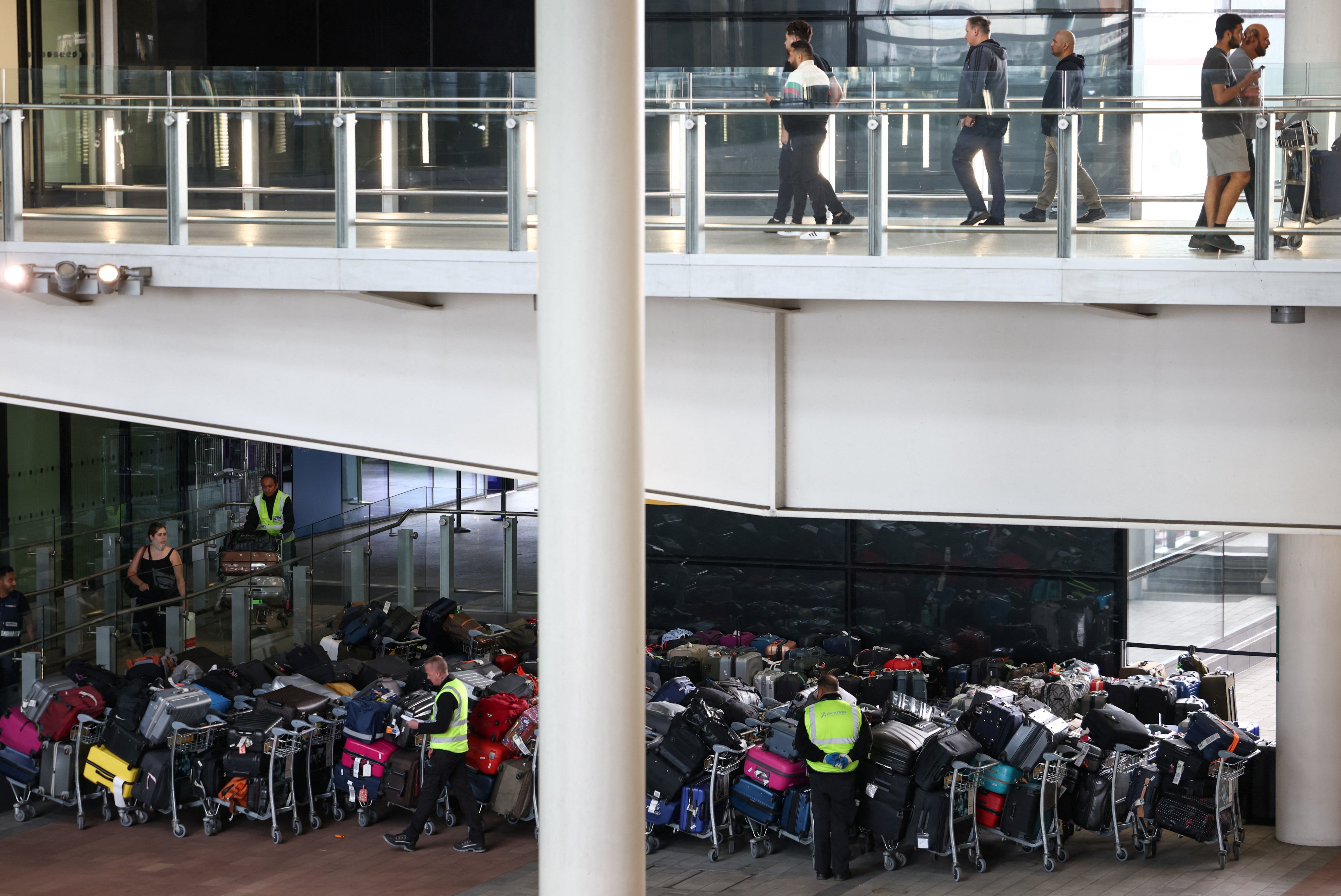 Airport workers stand next to lines of passenger luggage arranged outside Terminal 2 at Heathrow Airport