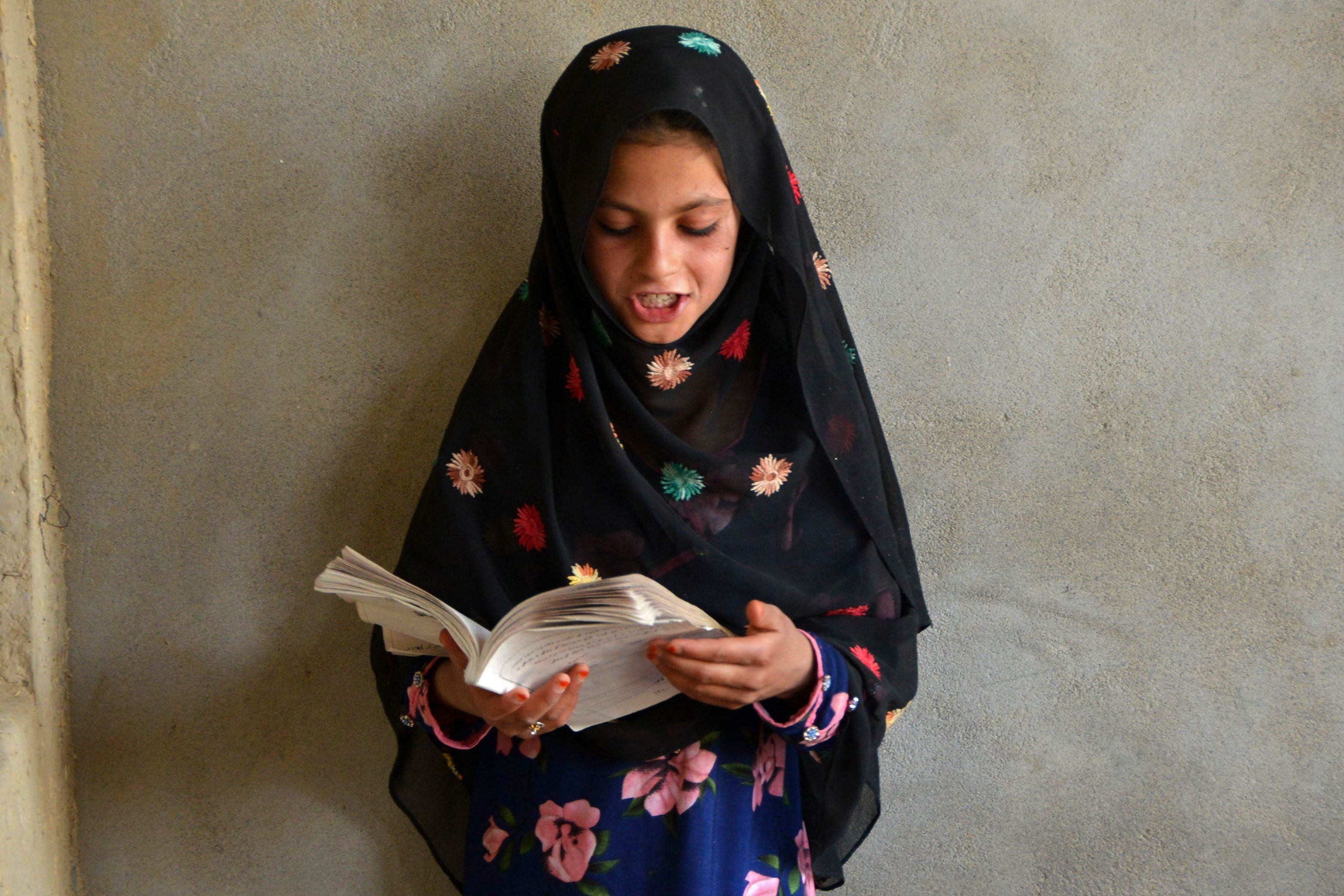 An Afghan girl reads a book inside a one-classroom private educational center in Panjwai district of Kandahar