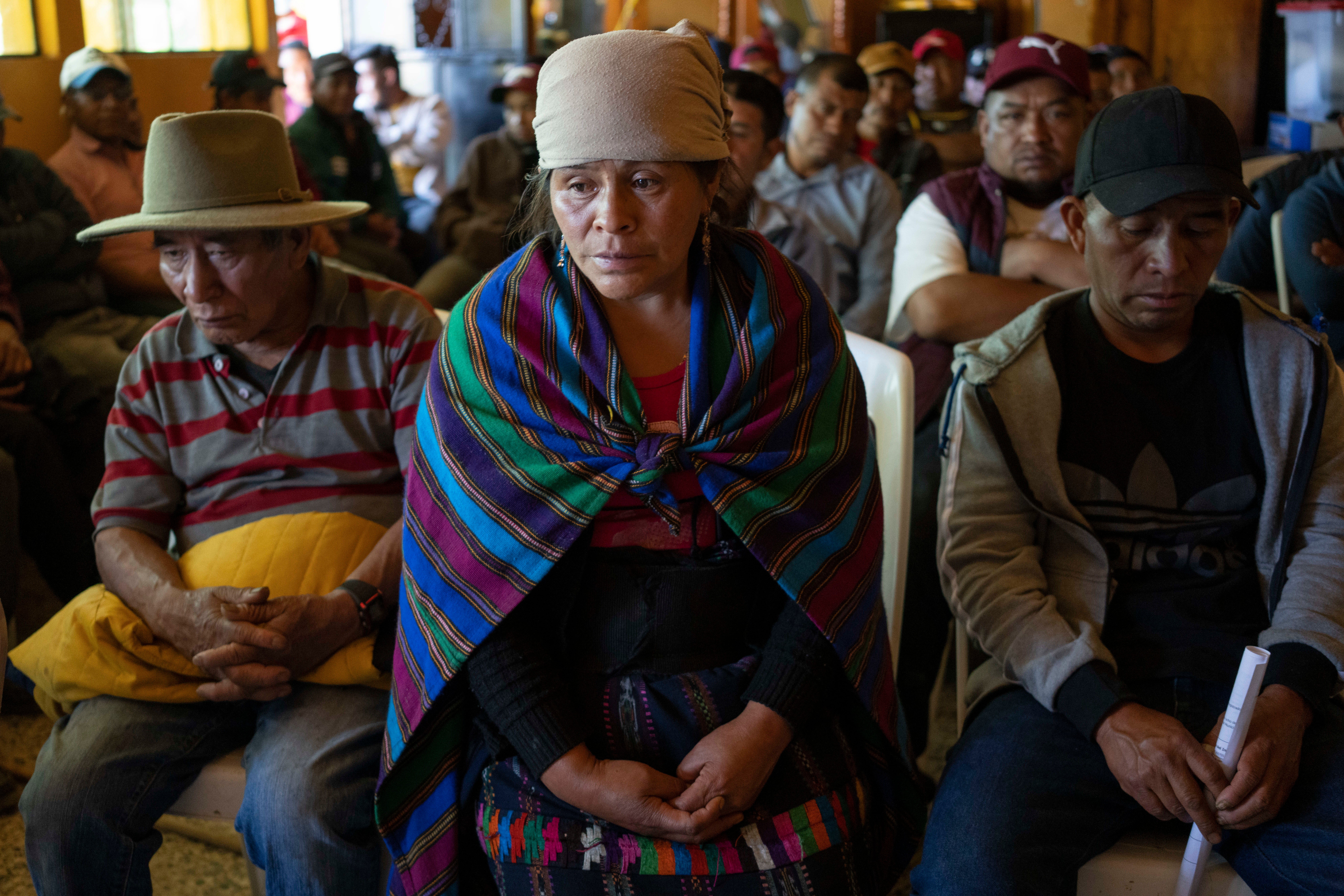 Magdalena Tepaz, center, and Manuel de Jesus Tulul, right, parents of Wilmer Tulul, wait for the start of a community meeting in Tzucubal, Guatemala