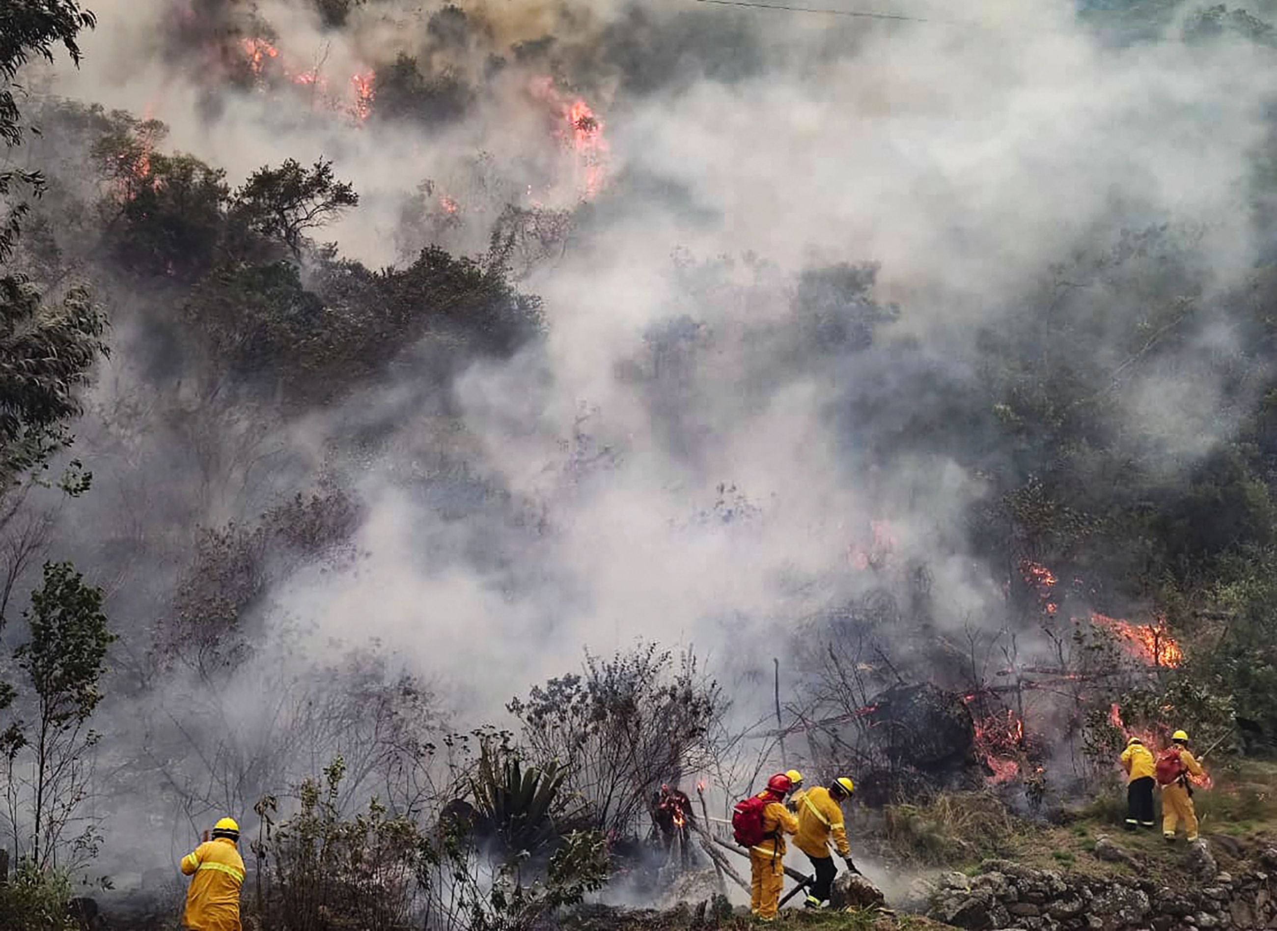 Firemen work to put out a fire in the bush surrounding the ruins of Llamakancha, a sector in the archaeological site of Machu Picchu.