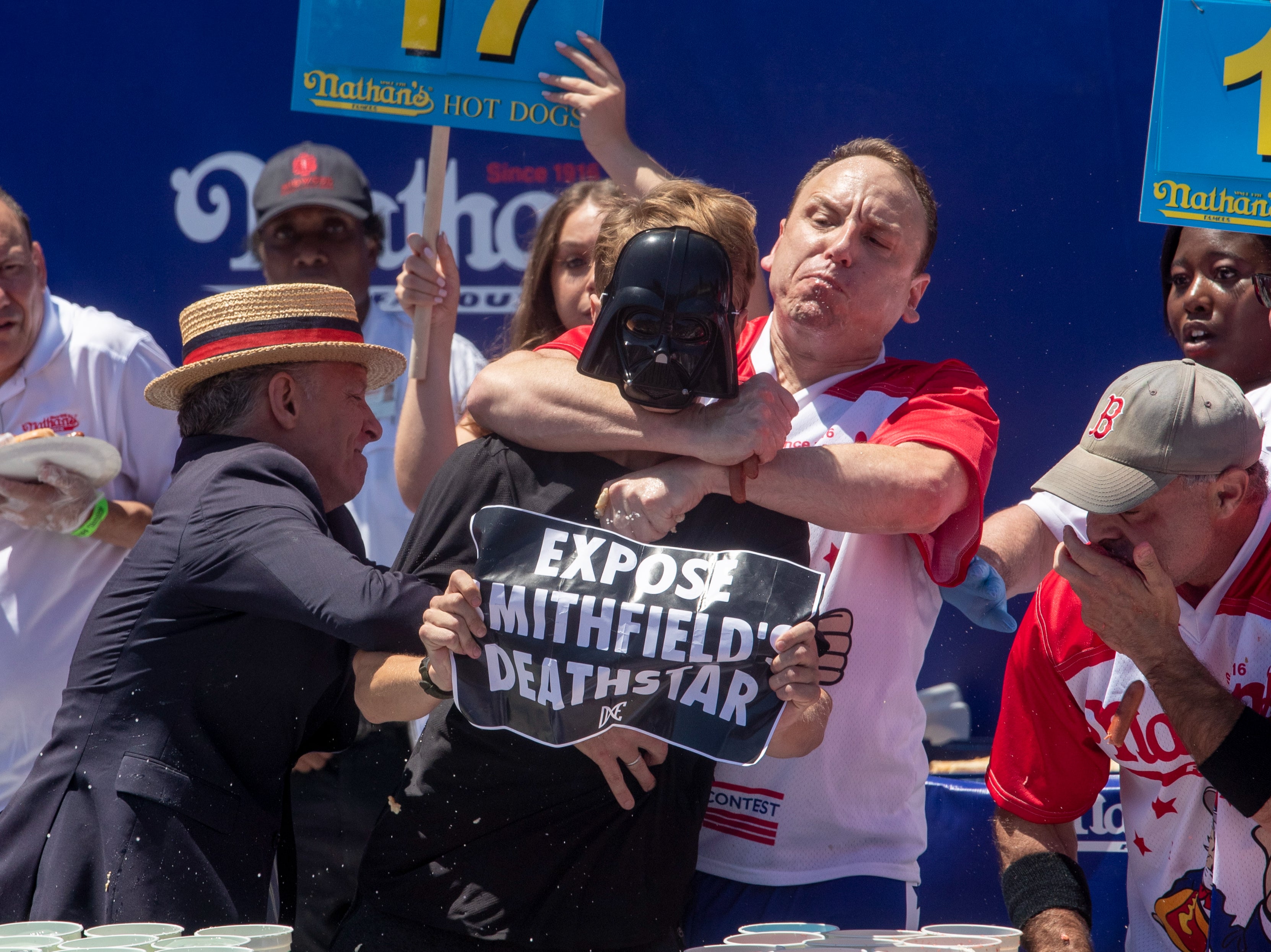 Top competitive eater Joey Chestnut (C) tackles a protester with a ‘Expose Mithfield’s Deathstar’ sign during Nathan’s Famous Fourth of July International Hot Dog Eating Contest at Coney Island in New York, New York, USA, 4 July 2022