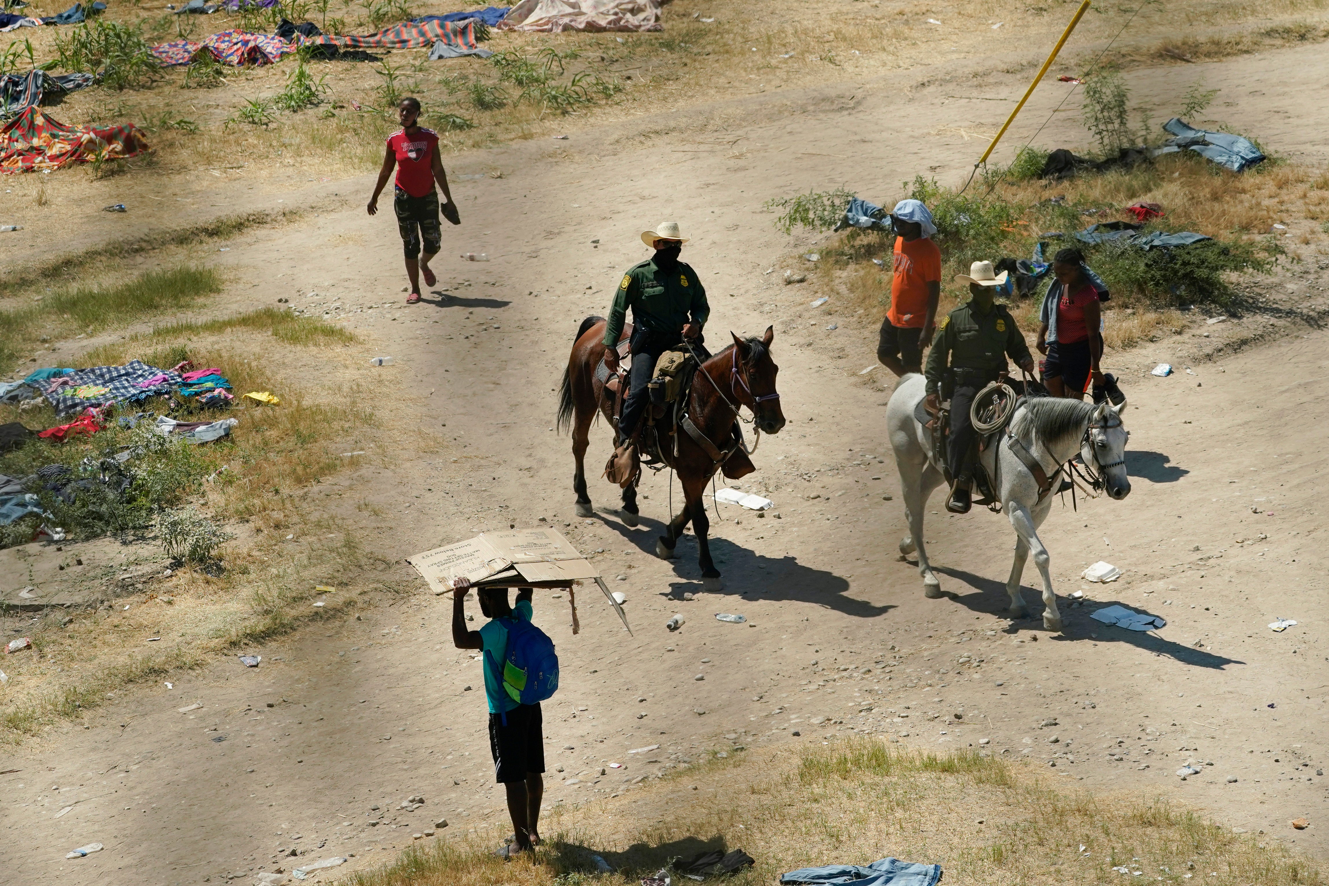 Border Patrol agents pass Haitian migrants at a makeshift camp, Sept. 17, 2021, in Del Rio, Texas