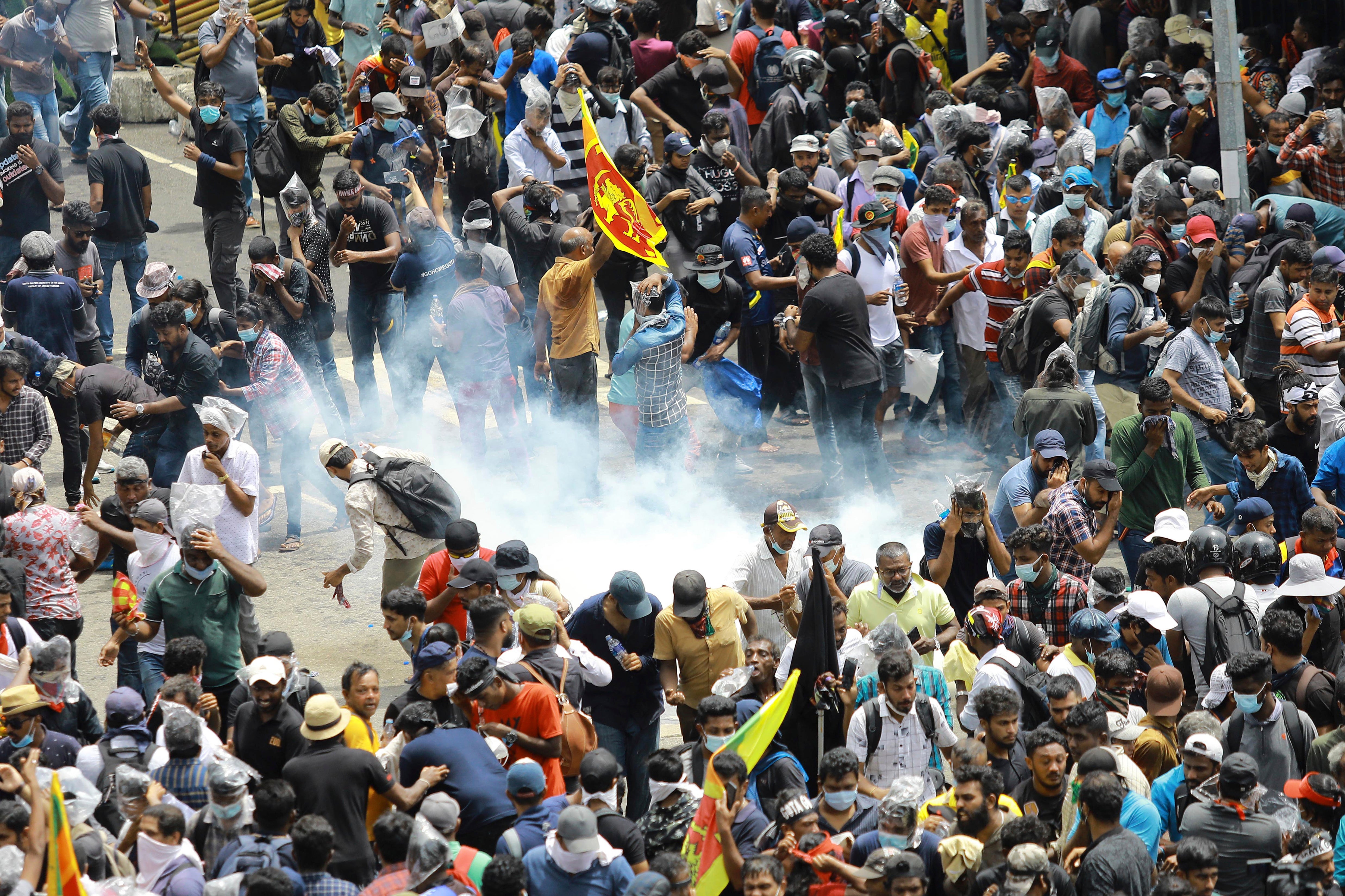 Protesters react as a teargas shell fired by police lands next to them in Colombo