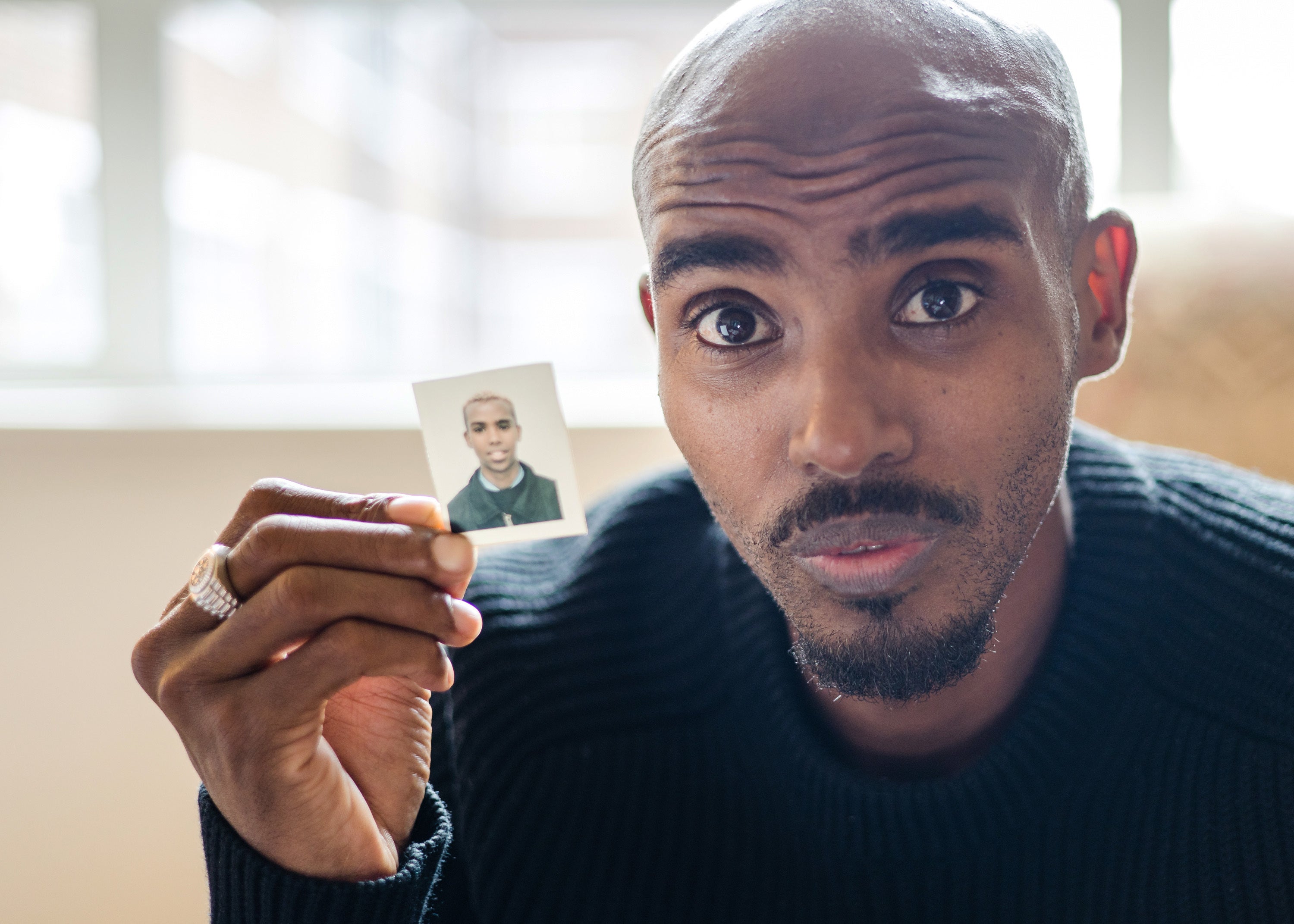 Sir Mo Farah holds up a photo of himself as a child