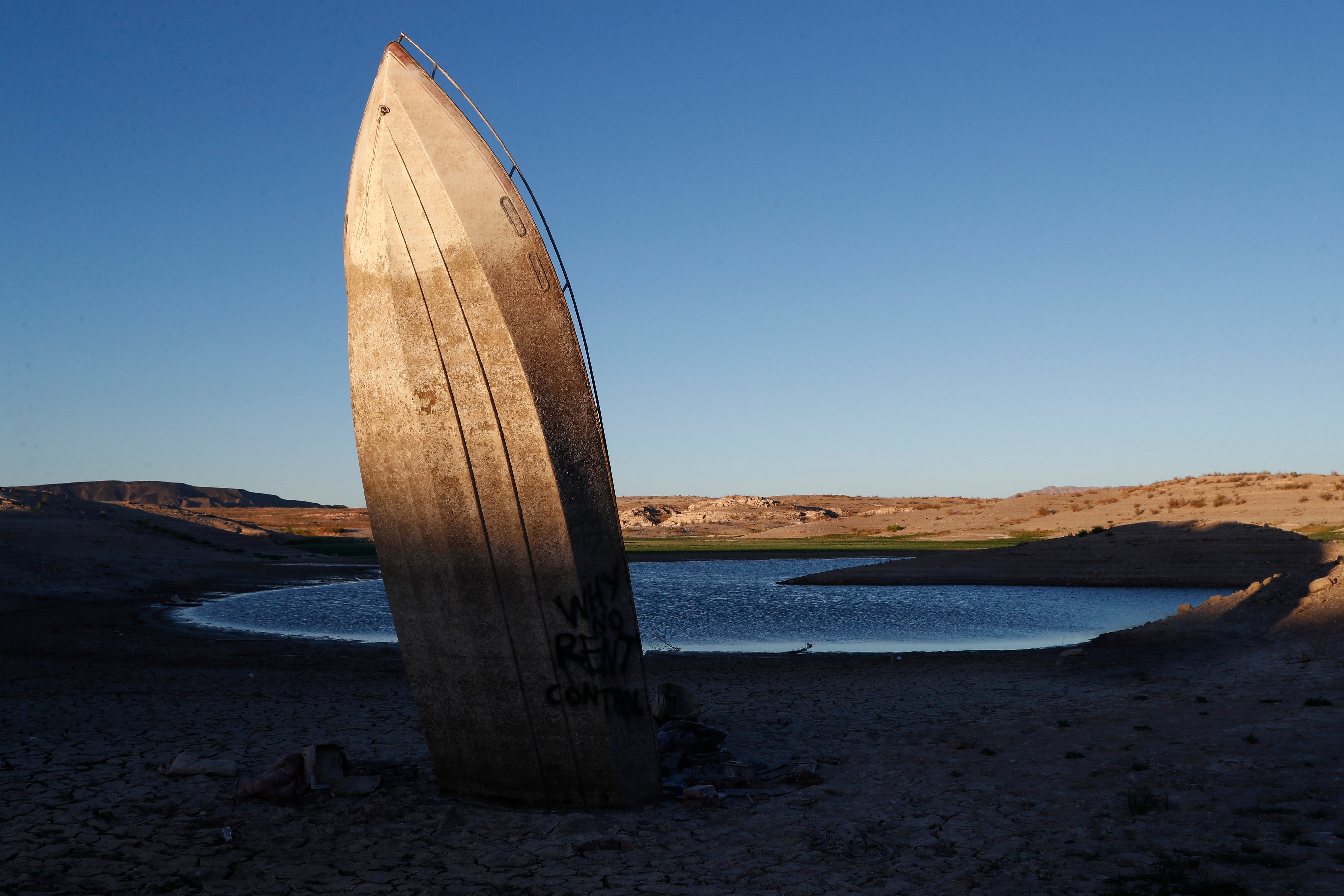 A beached boat sticks up in the sand on the shores of the lake