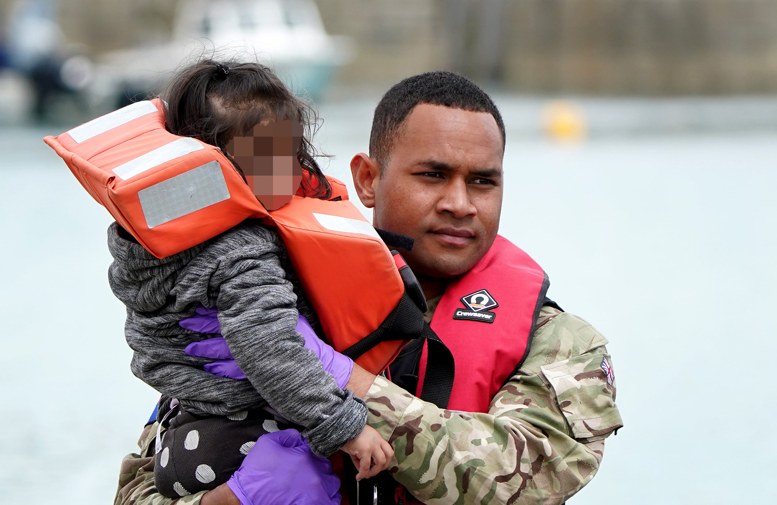 A young child is carried by a military officer as a group of people thought to be migrants are brought in to Dover, Kent, following a small boat incident in the Channel (Gareth Fuller/PA)