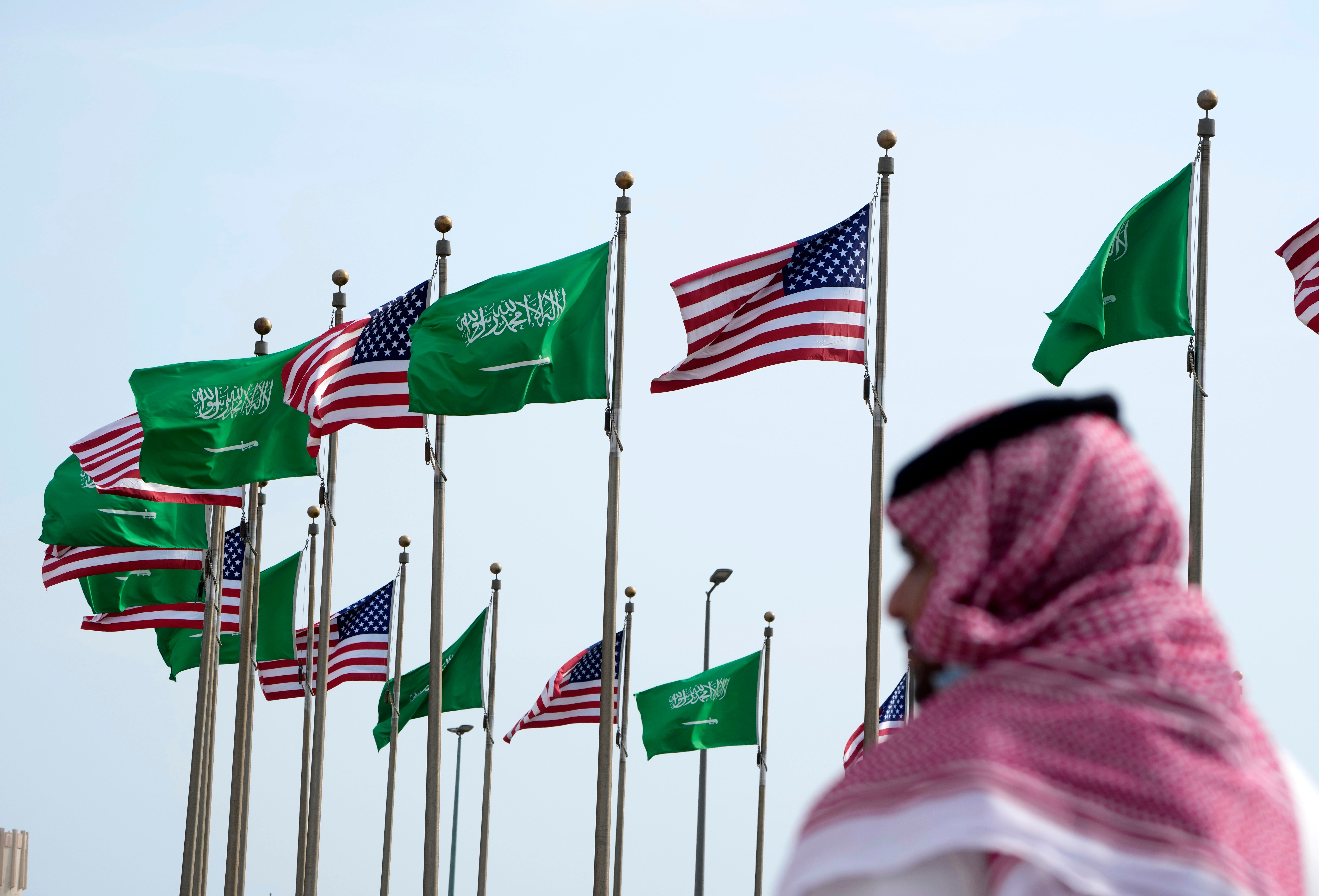 A man stands under American and Saudi Arabian flags prior to a visit by US president Joe Biden, at a square in Jeddah, Saudi Arabia, Thursday, 14 July 2022