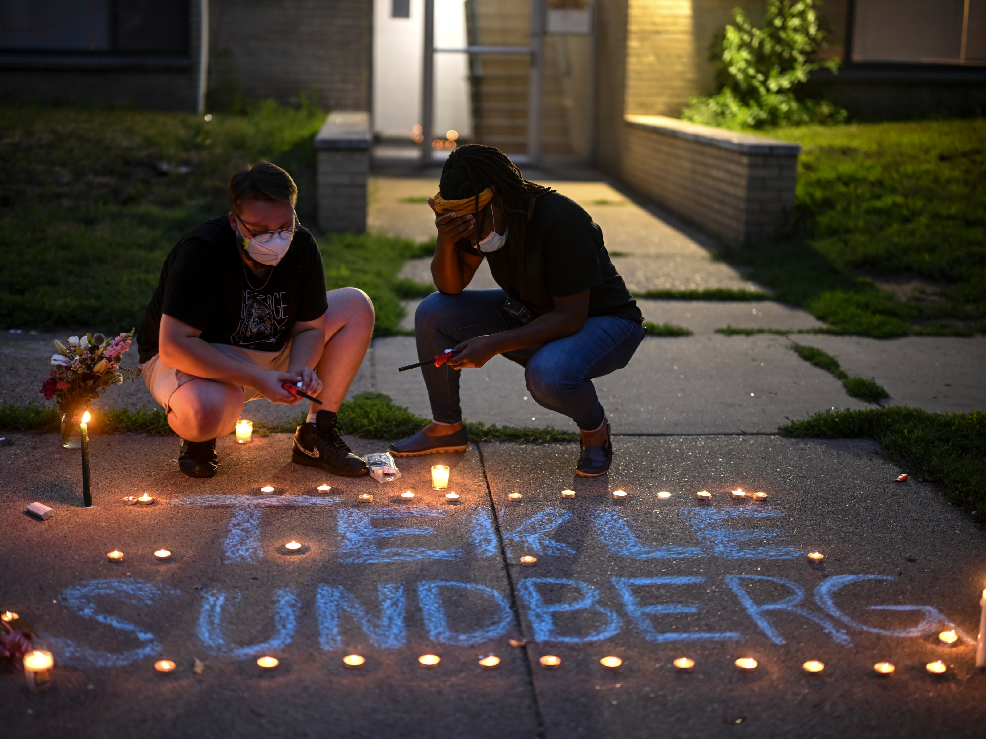 Marcia Howard, activist and George Floyd Square caretaker, right, takes a moment as she lights candles during a vigil for 20-year old Andrew Tekle Sundberg Thursday, July 14, 2022 outside the apartment building where he was killed