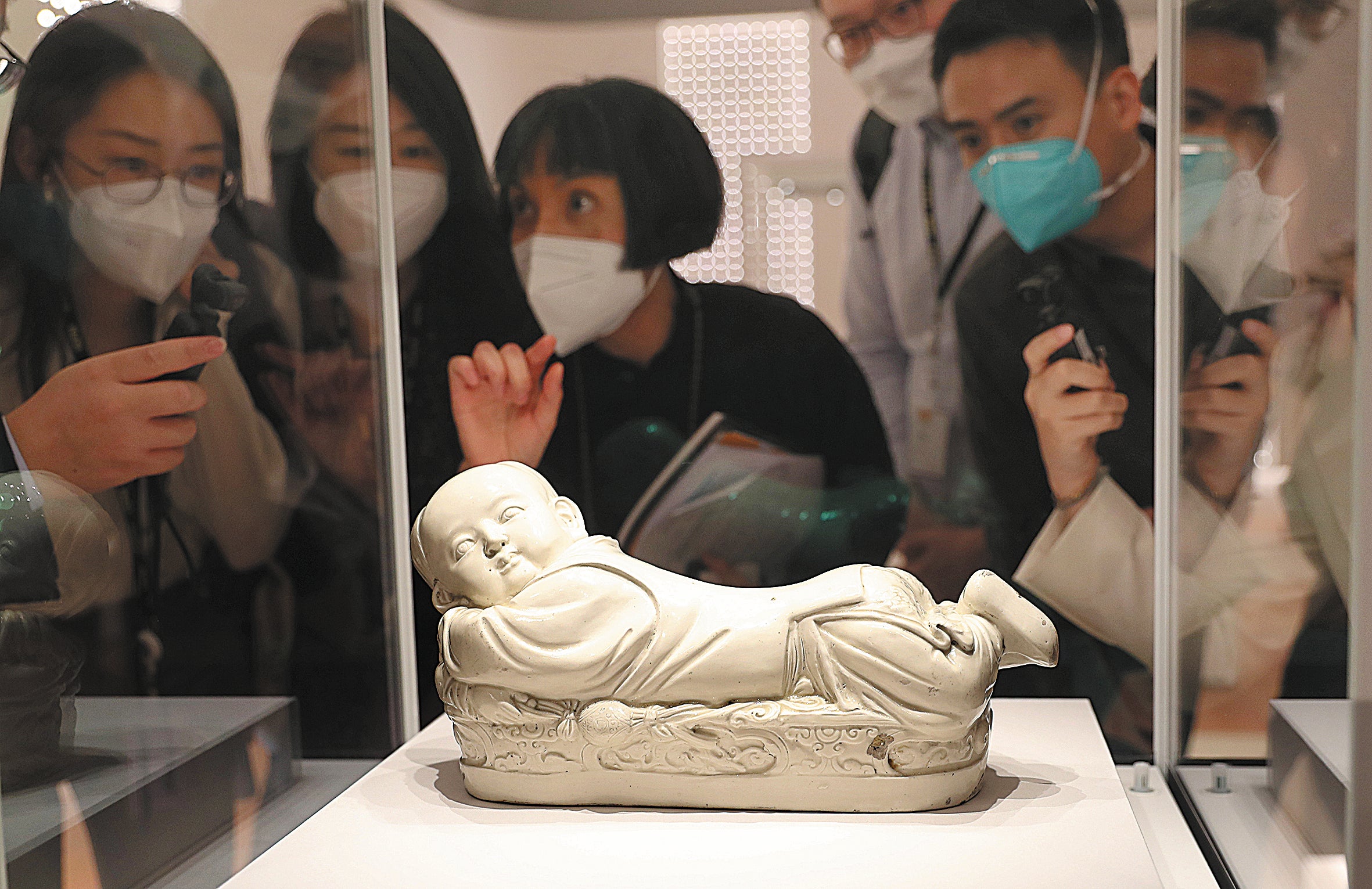 Visitors admire a white-glazed ceramic pillow featuring a boy lying on a couch, a rare artefact dating to the Song Dynasty (960-1279), at the Hong Kong Palace Museum