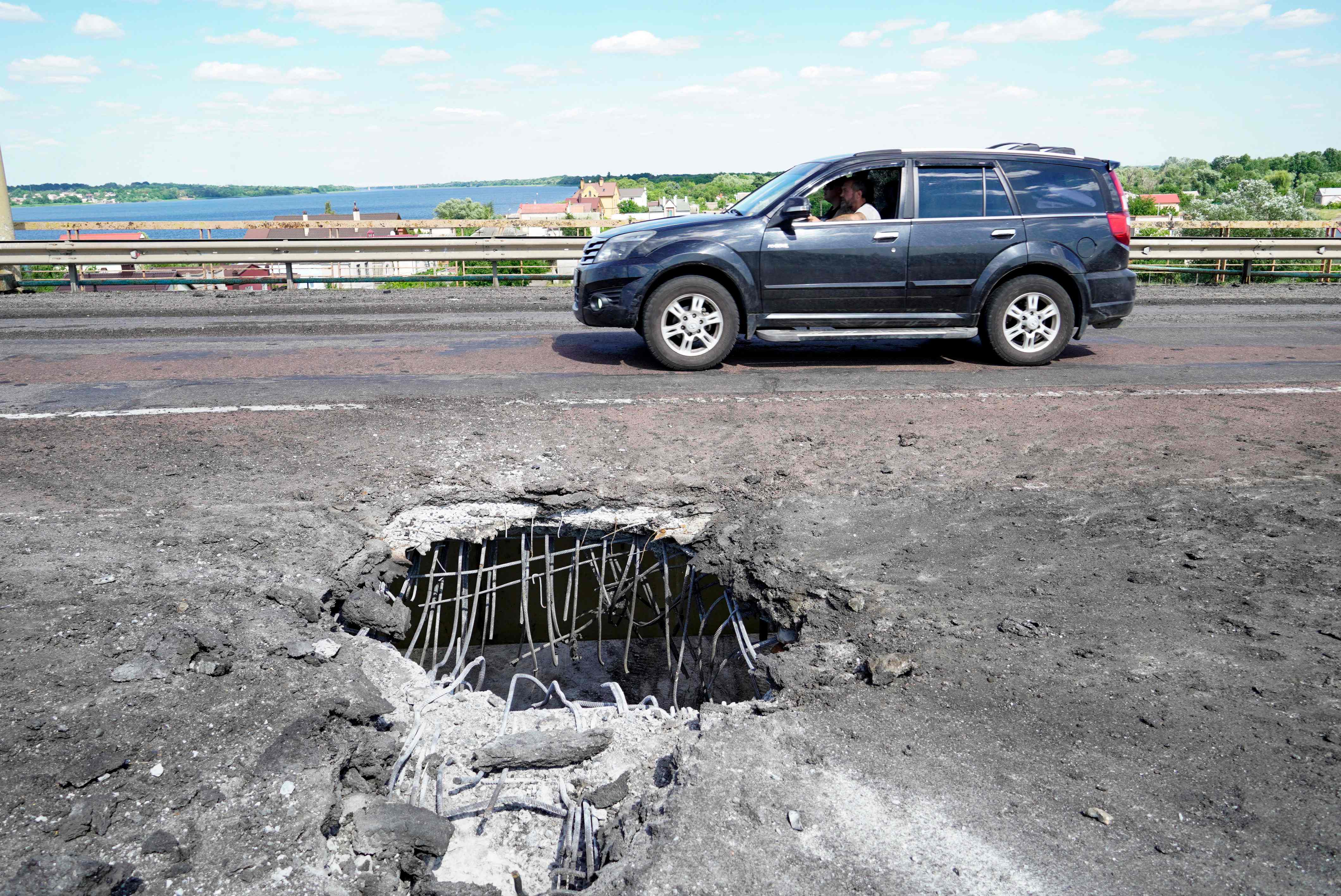 A car moves past a crater from a Ukrainian rocket strike on Kherson’s Antonovsky Bridge across the Dnipro River