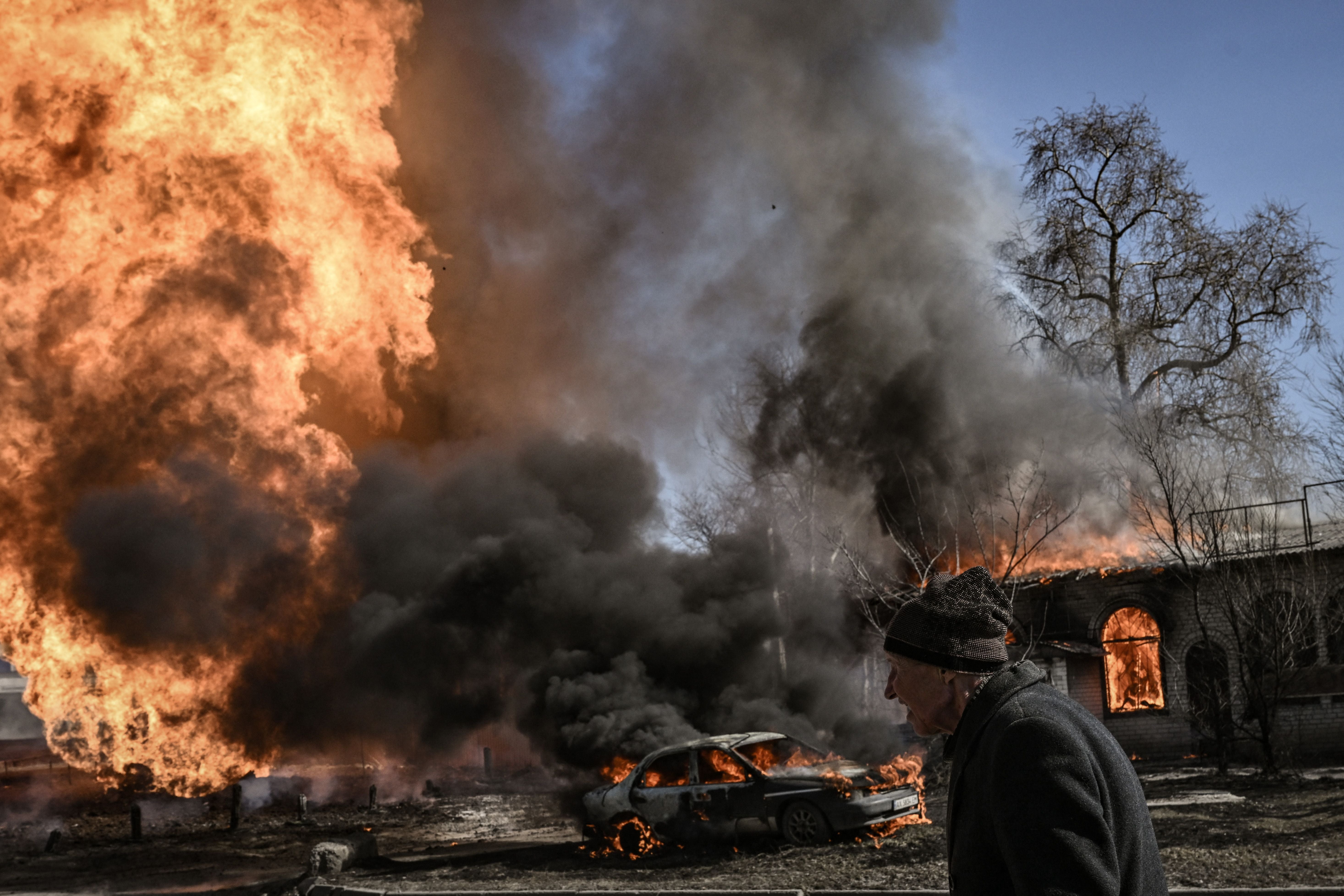 A Ukrainian woman walks past a building on fire following a Russian attack on Kharkiv