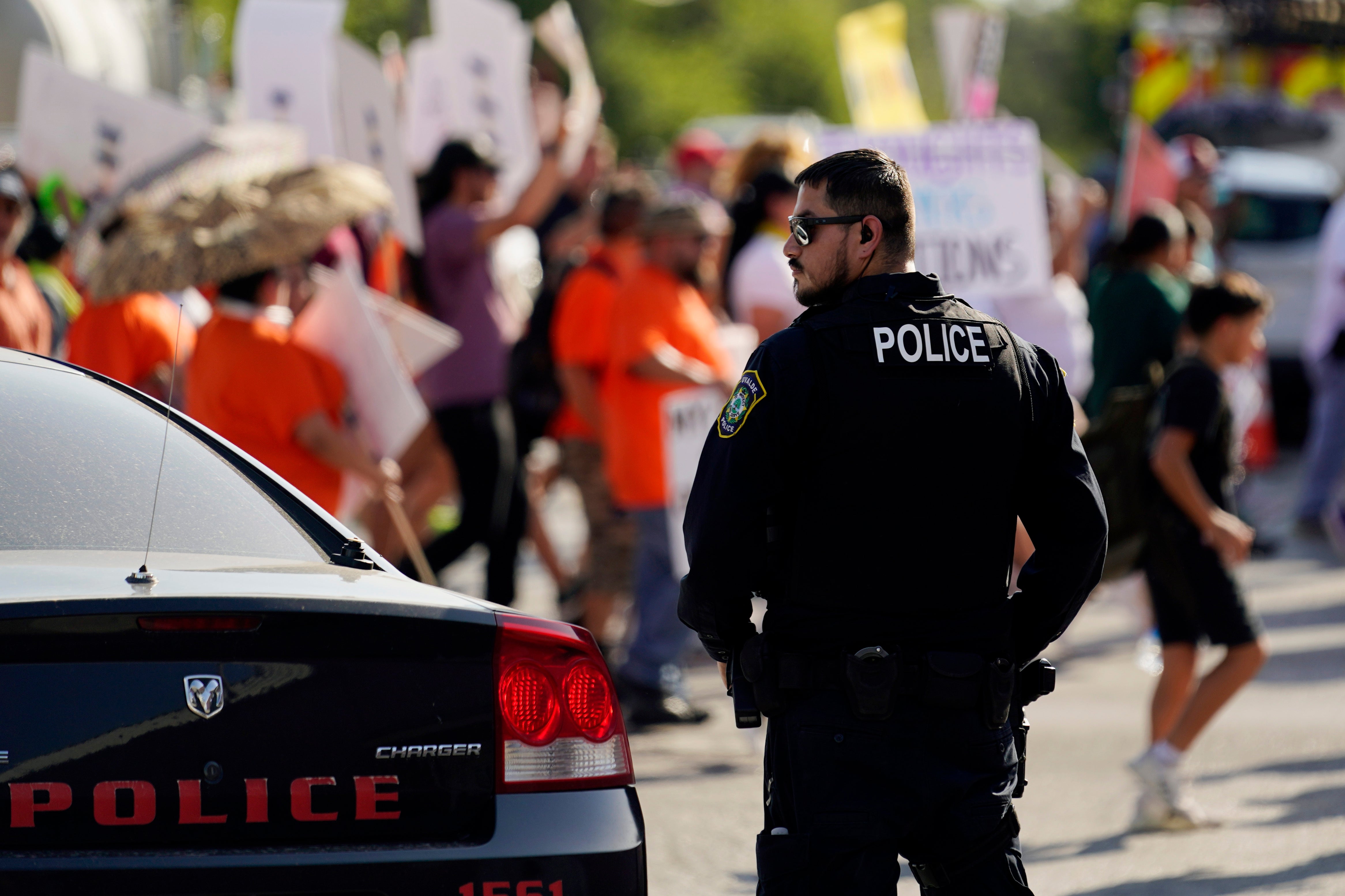 A Uvalde police officer watches as victims’ families demand answers and accountability