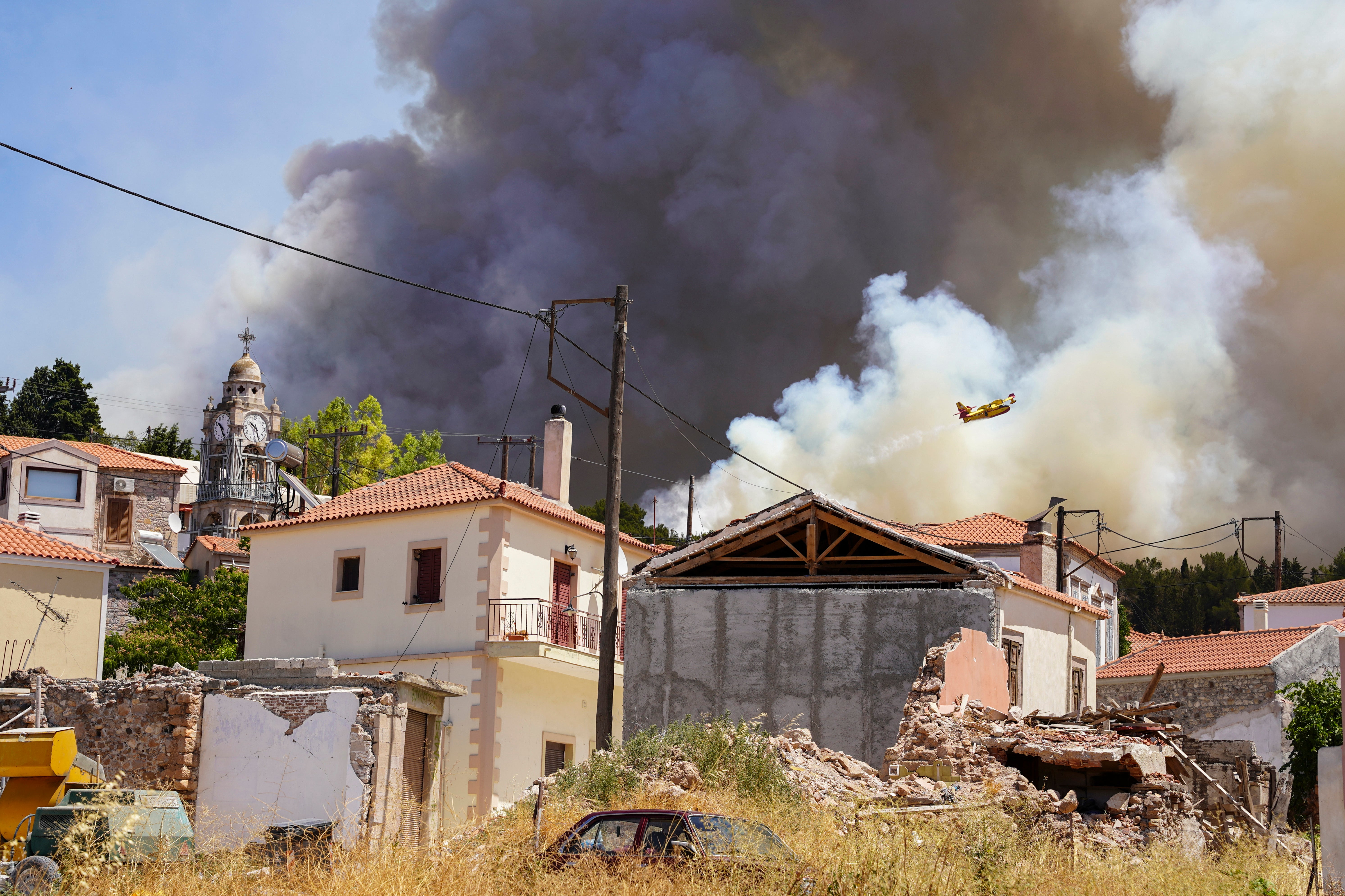 A firefighter aircraft drops water over a forest fire as smoke rises near Vrisa village