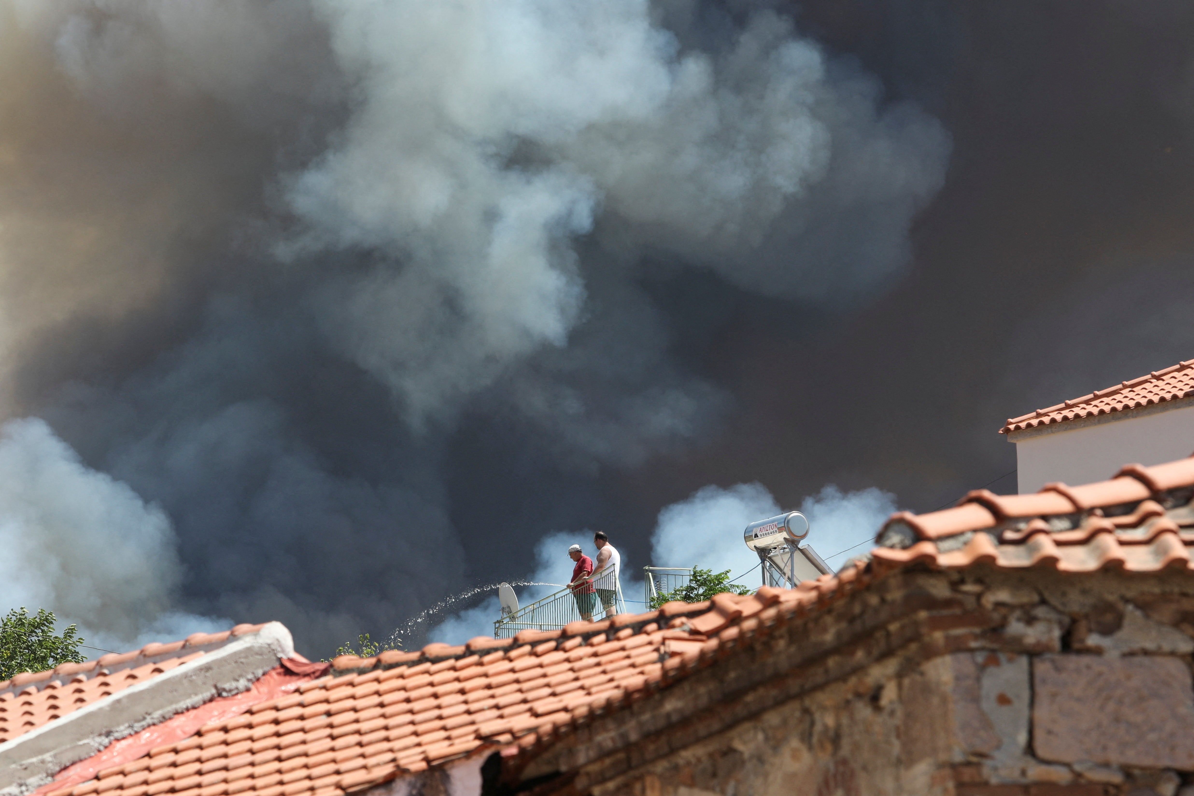 A Local sprays water as wildfire burns at the village of Vrisa, on the island of Lesbos, Greece