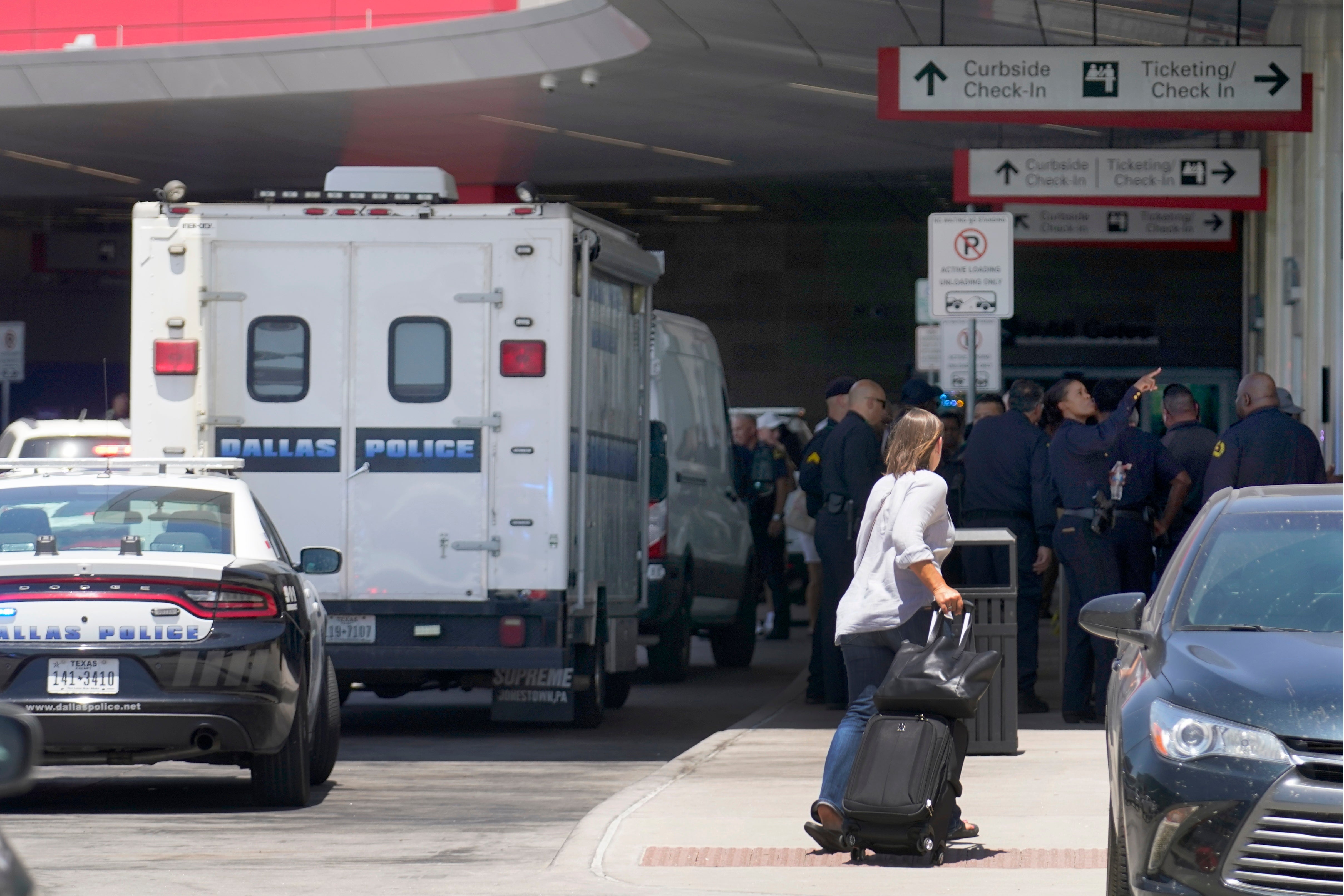 A traveler makes her way past emergency responders standing outside the ticketing and check in area at Dallas Love Field in Dallas, Monday, July 25, 2022