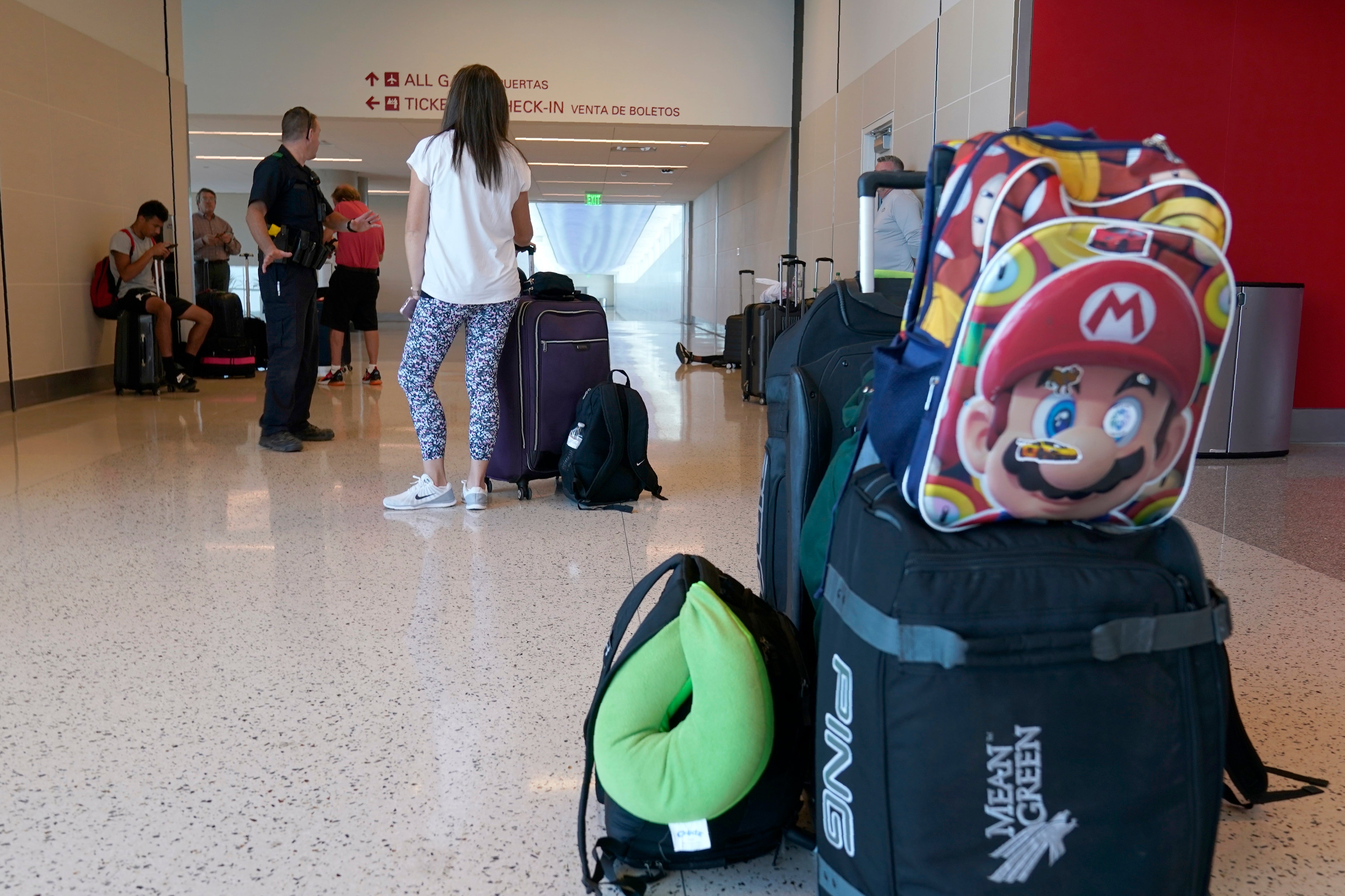 A Dallas police officer, left, talks with travelers as he ask them to wait in a walkway leading to the terminal at Dallas Love Field in Dallas, Monday, July 25, 2022