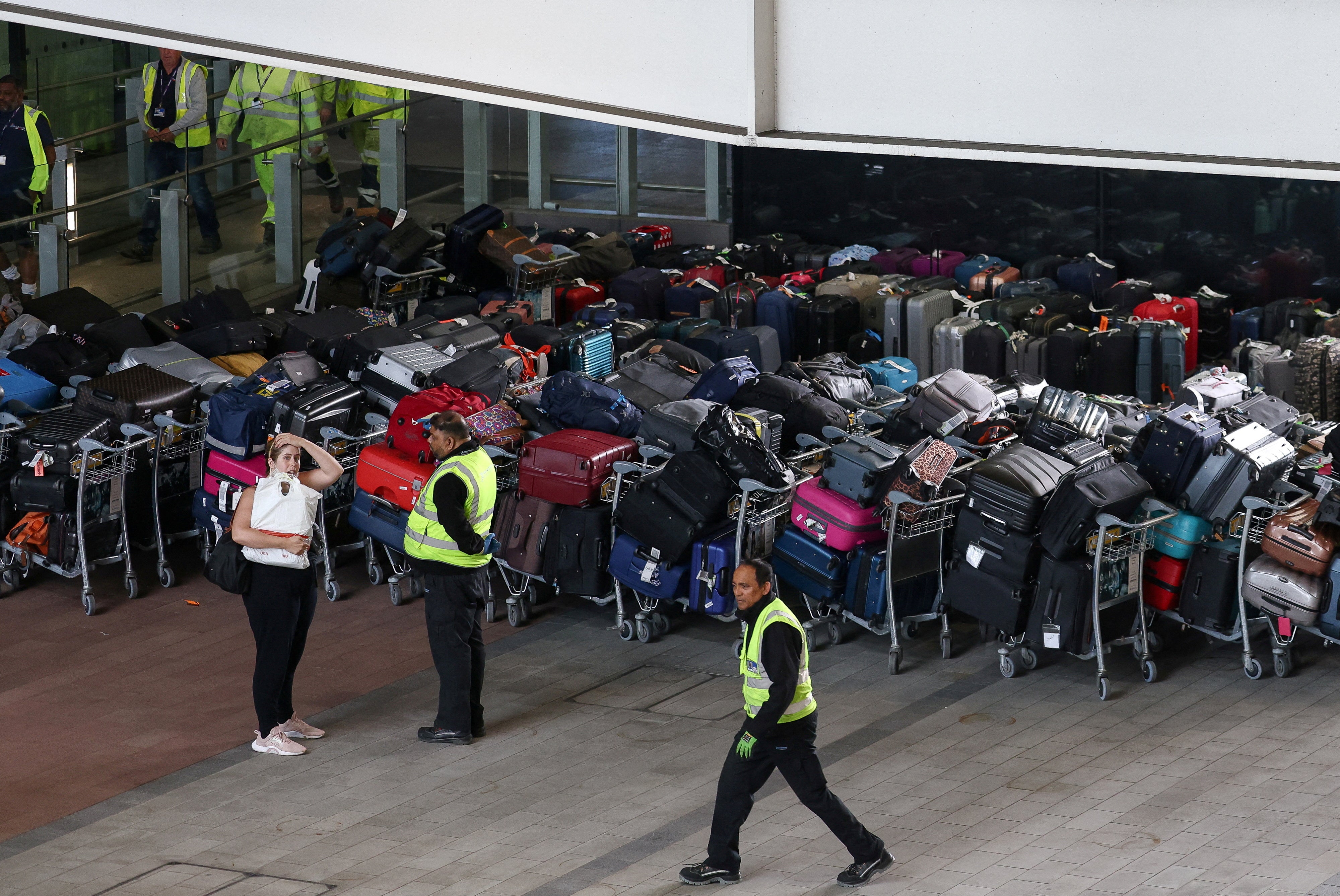 Airport workers stand next to lines of passenger luggage