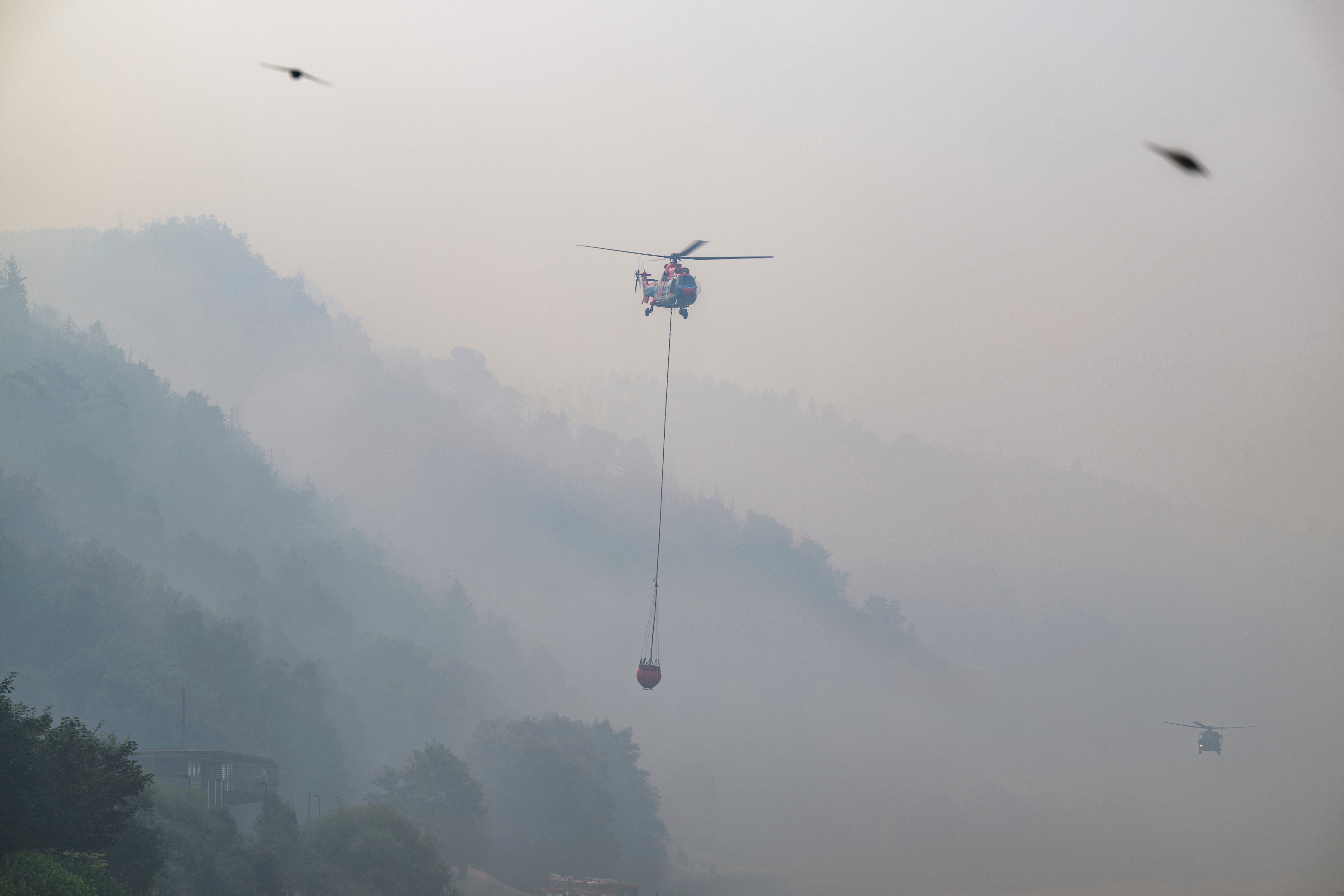 A cargo helicopter from Austria takes water from the Elbe River with an external water tank to extinguish a fire