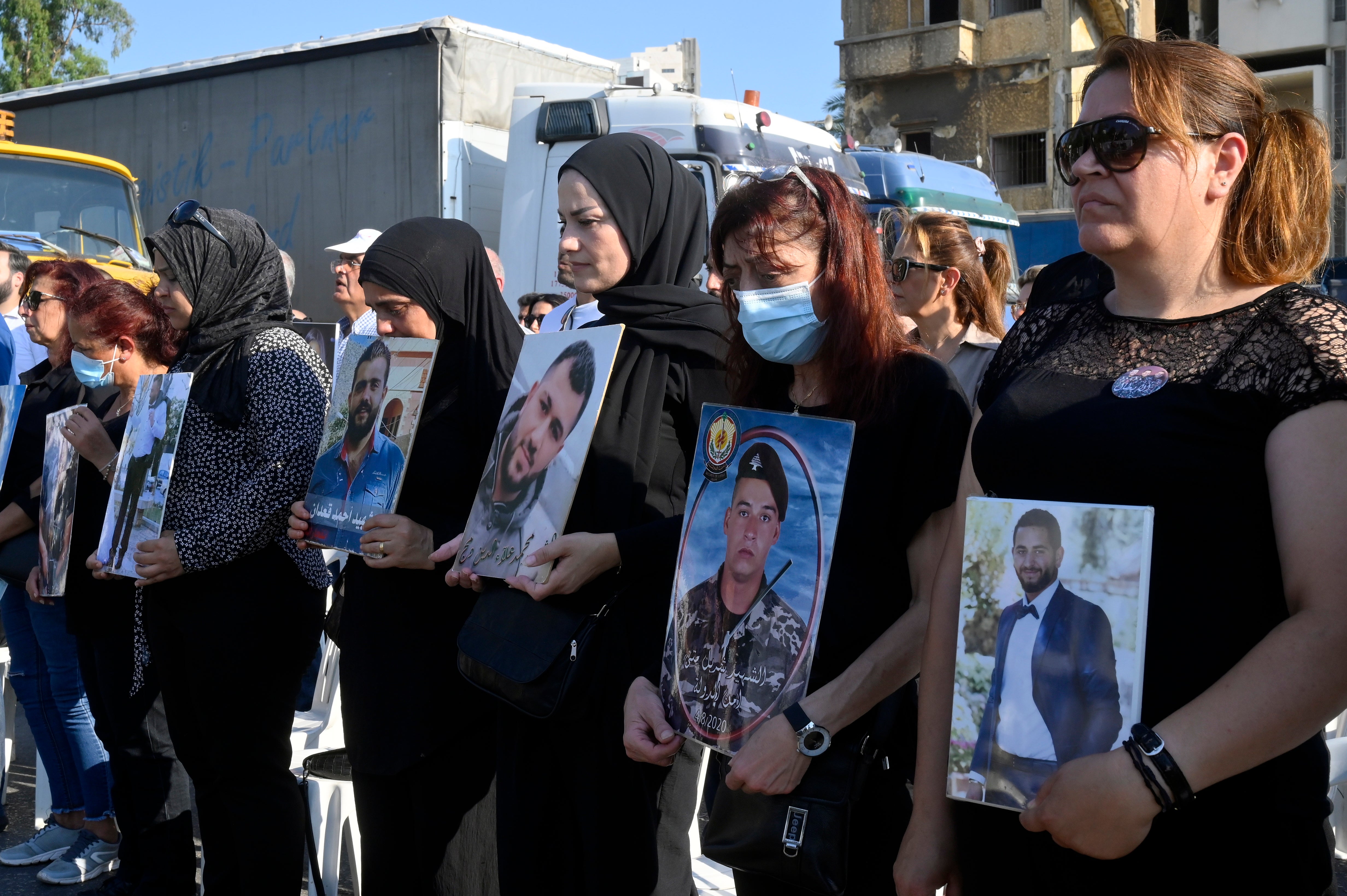 Families of victims of the 04 August Beirut port explosion carry portraits of their deceased relatives outside the devastated harbour during a protest