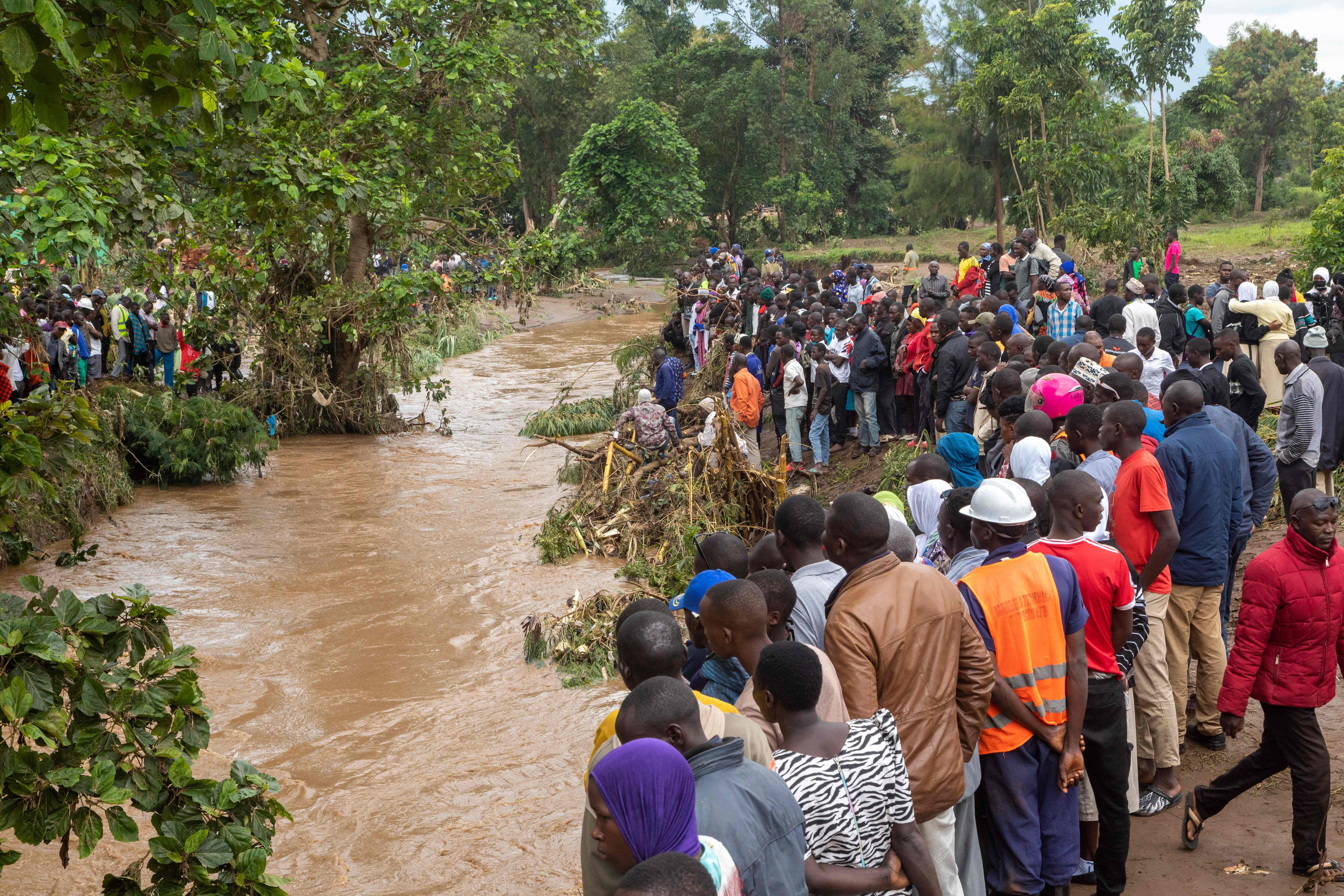 Onlookers watch as people search for flood victims at the Nabuyonga River in Uganda on Tuesday