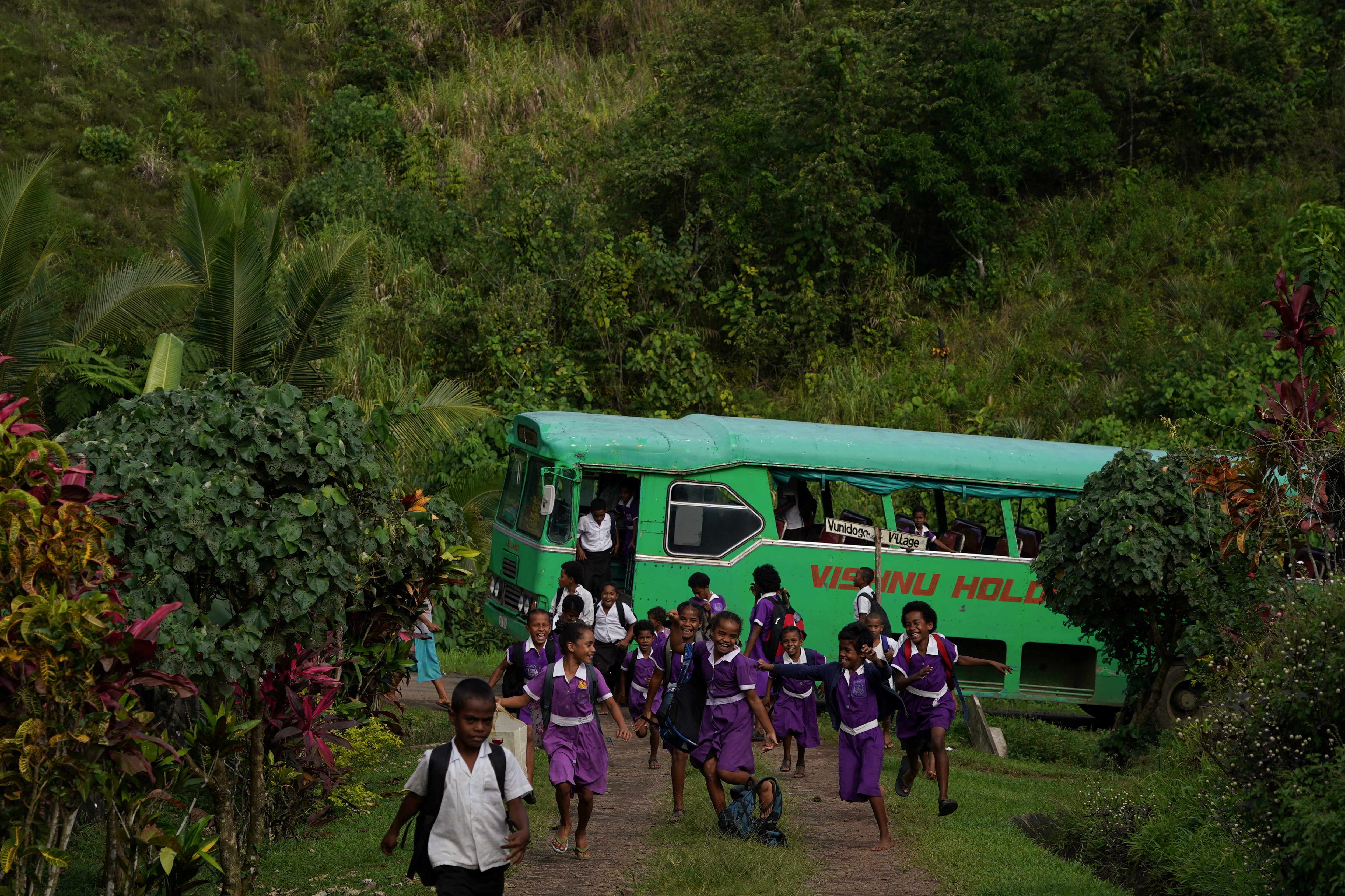 Children get off a school bus as they return home for the day to the new relocated site of Vunidogoloa village