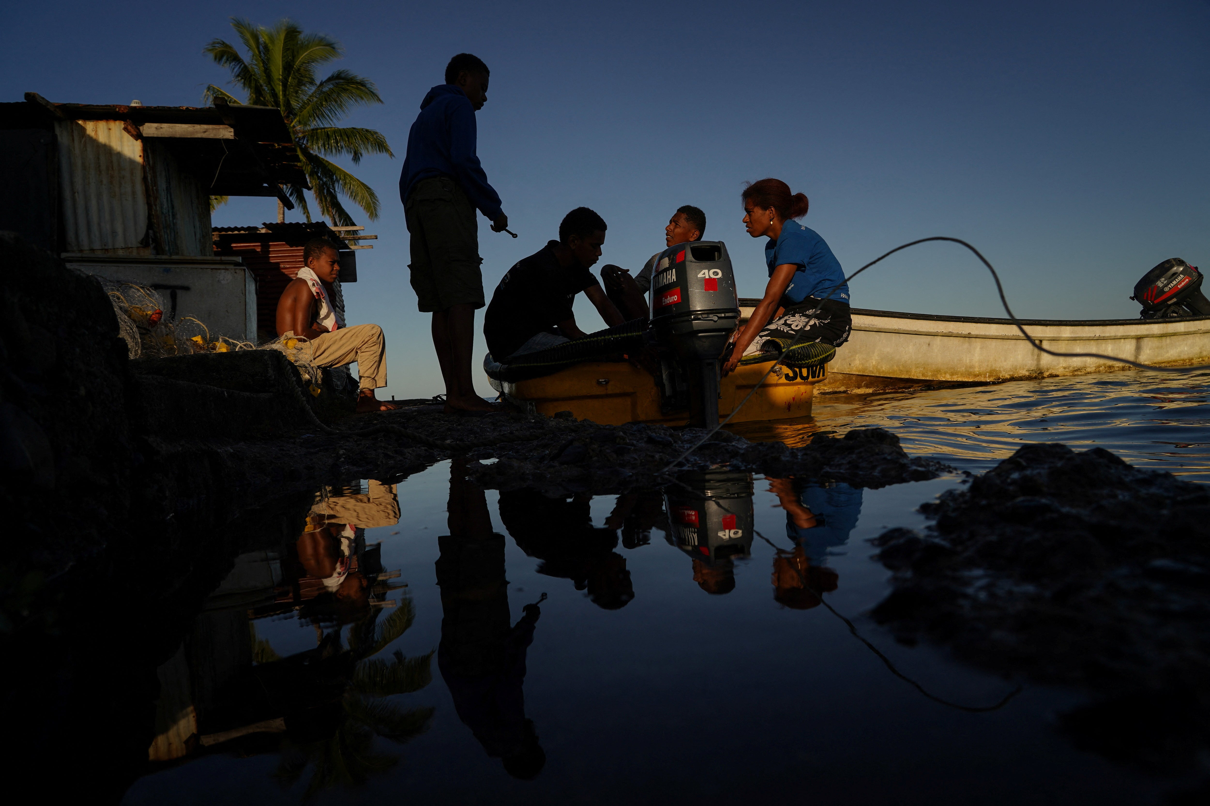 Local students Jona Togaciri, Talikai Kavu, Semisi Dradra, Tavaga Dradra and Joanna Dradra gather at the edge of a flooded seawall during high tide, while working on a boat motor in Serua village