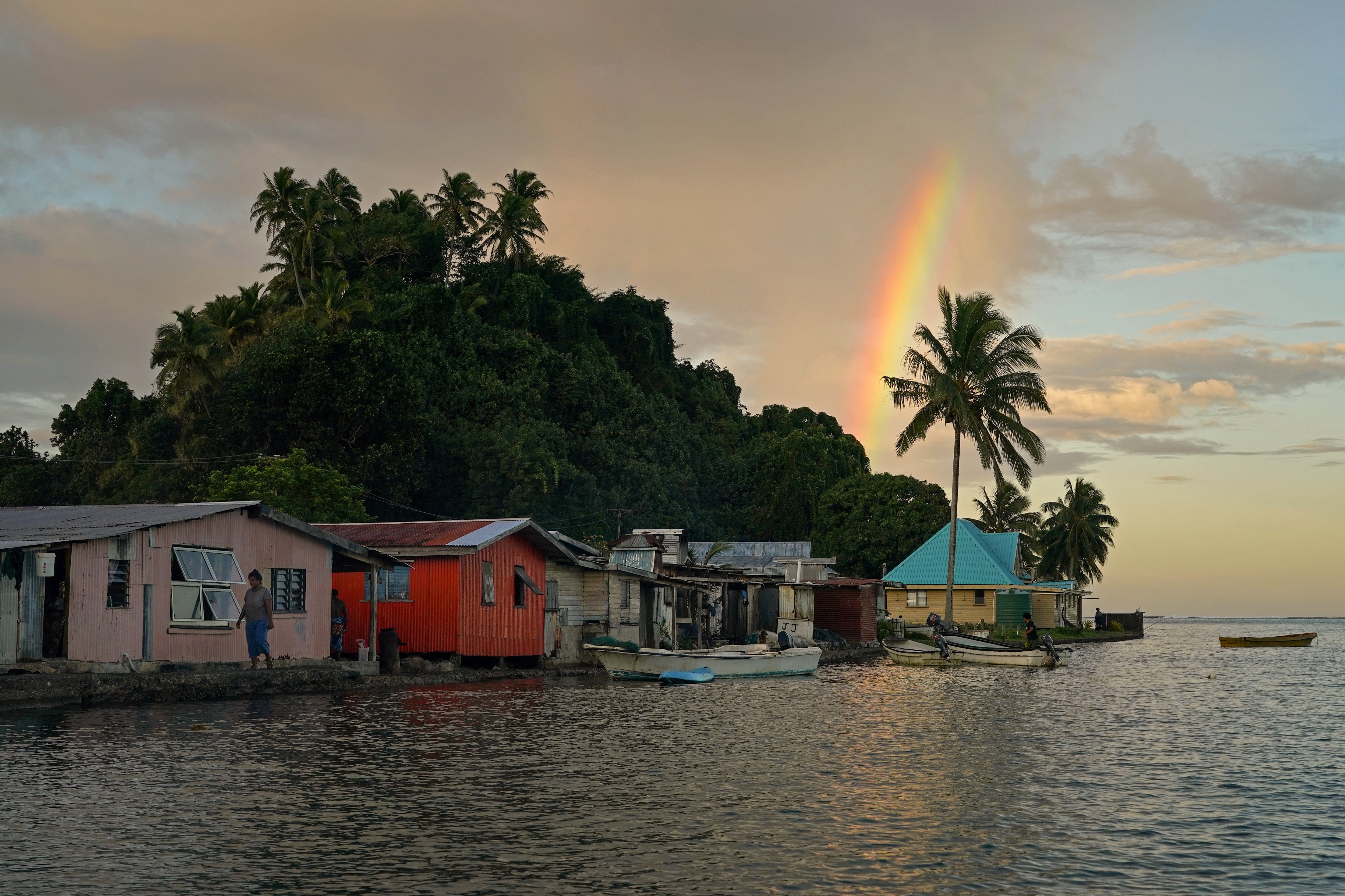 Local resident Tarusila Boseiwaqa walks along a seawall that no longer protects homes from the intrusion of water at higher tides, as a rainbow forms over Serua village