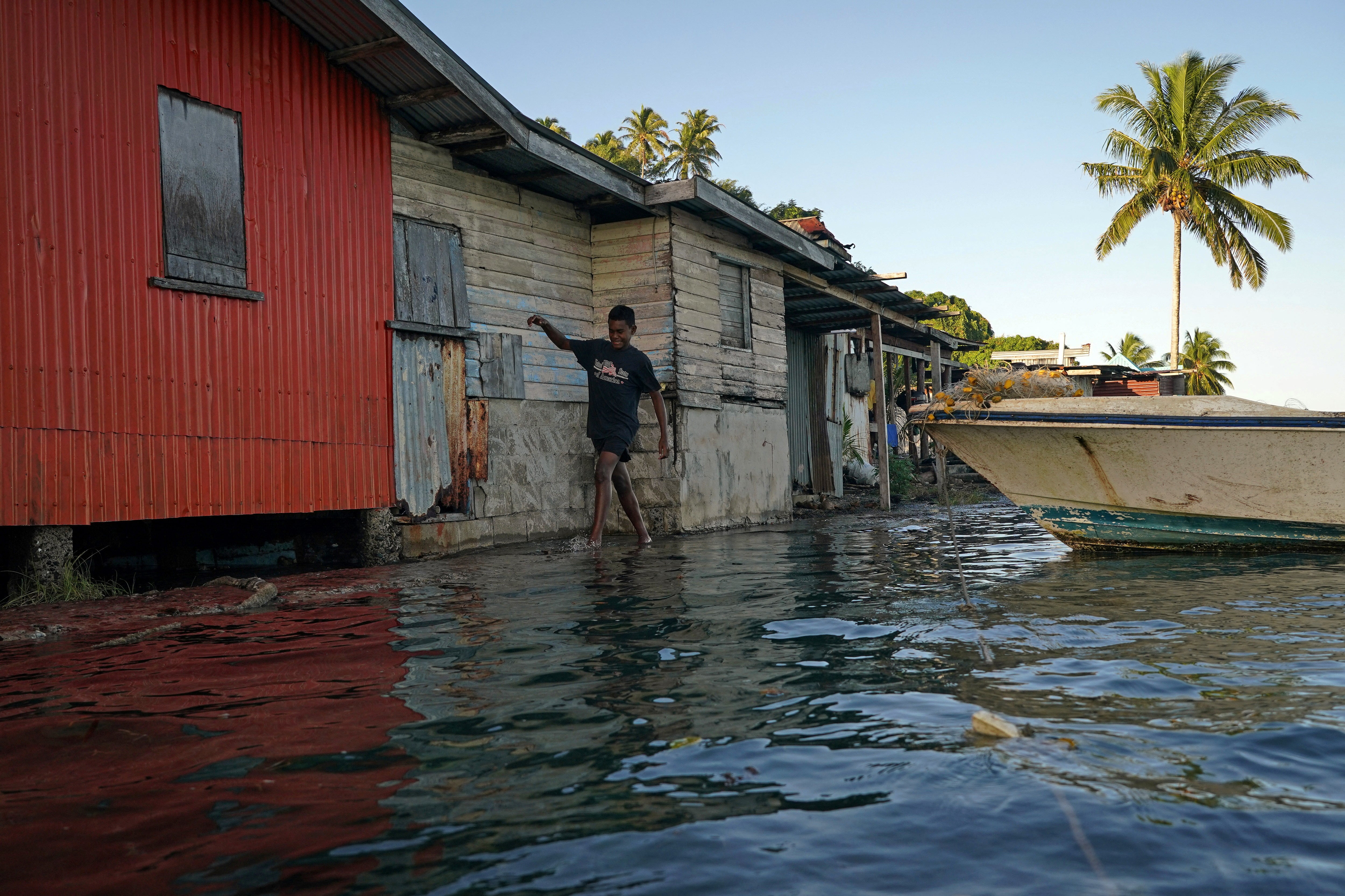 Local boy Ratusela Waqanaceva, 14, wades through seawater flooding over an ineffective seawall at high tide