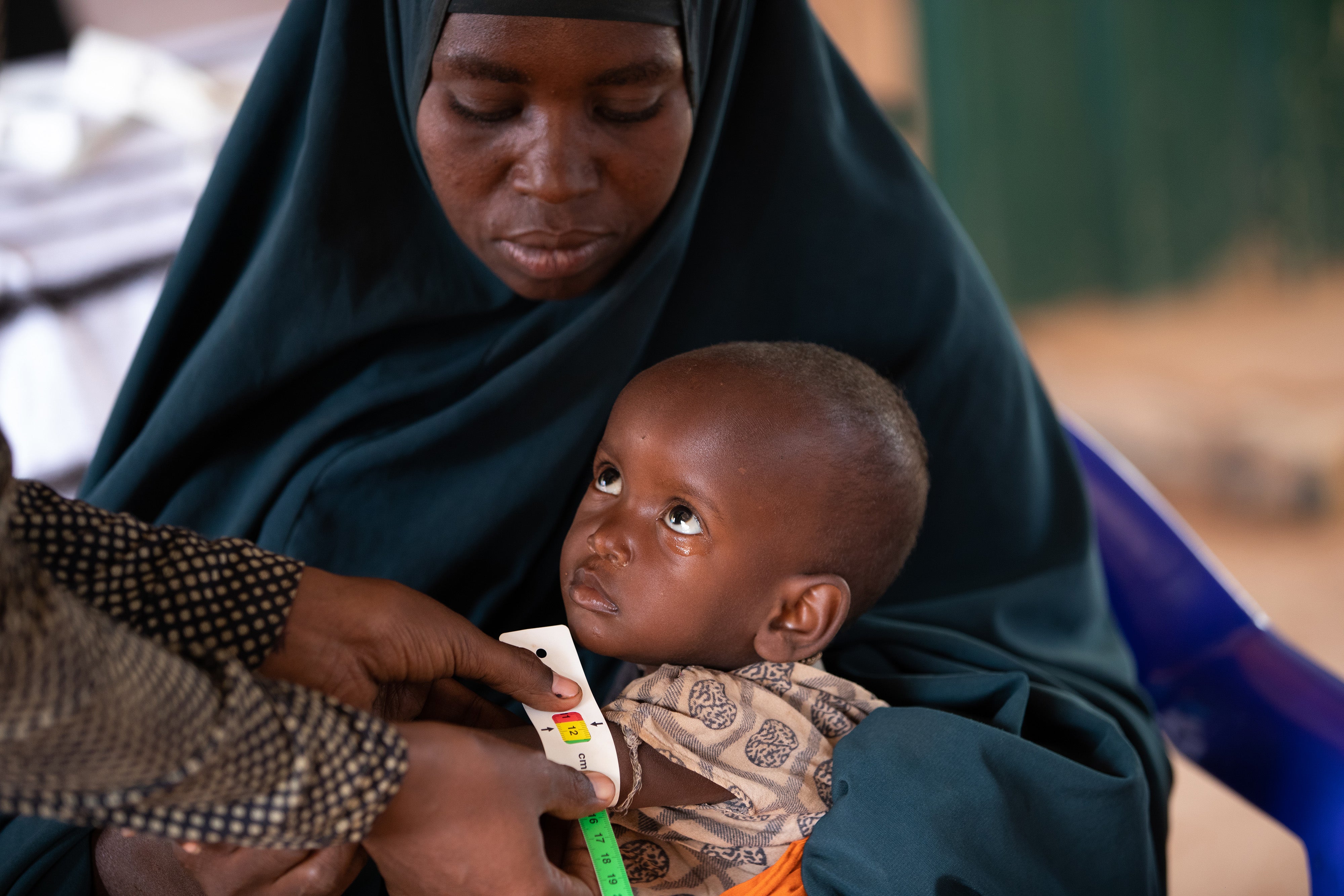 Mashallah, two, is held by his mother Dahera while his MUAC is measured and he is assessed for malnutrition