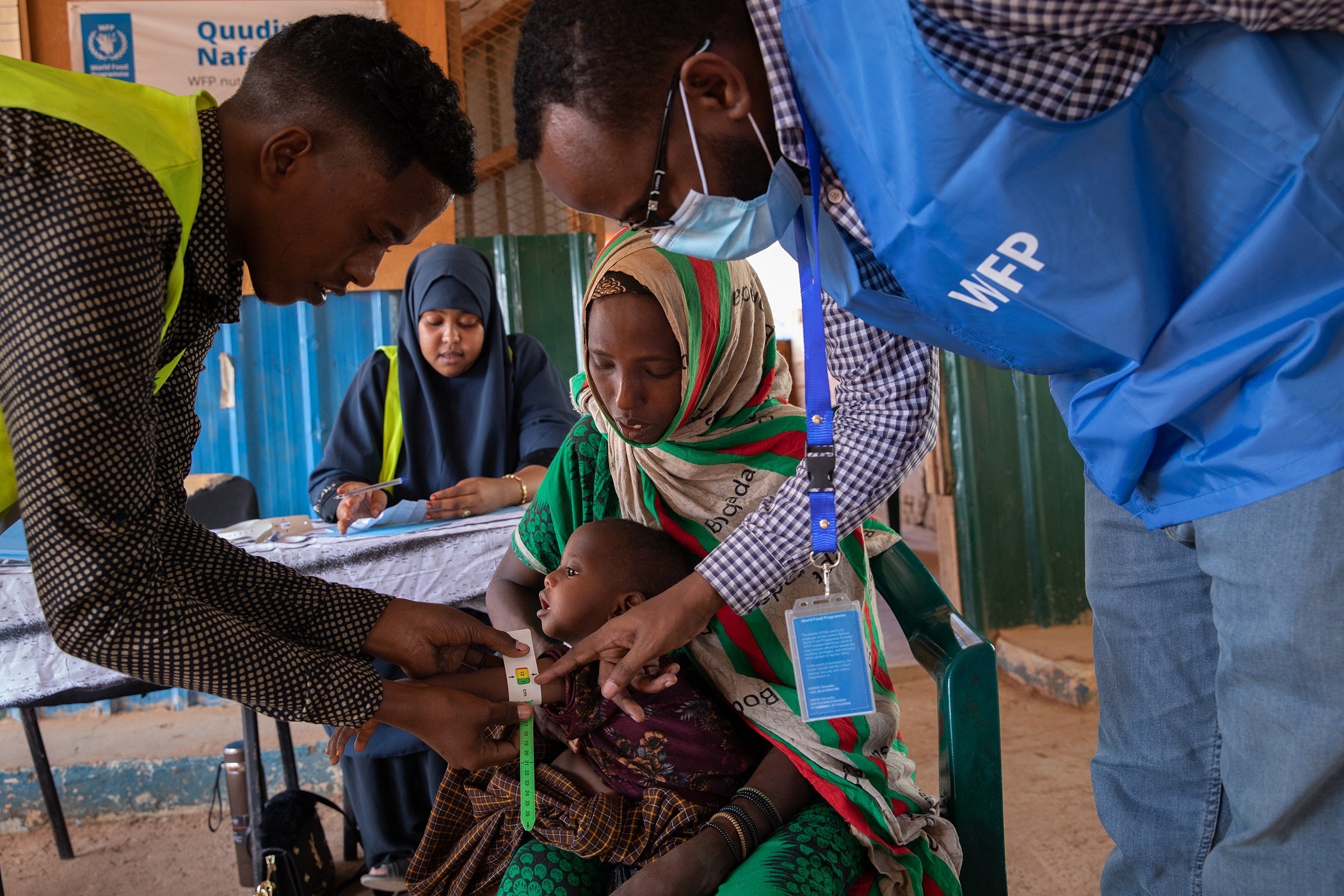 Mido holds Fatun while her mid-upper arm circumference (MUAC) is measured. Fatuna’s MUAC measurement confirms that she is suffering from moderate acute malnutrition