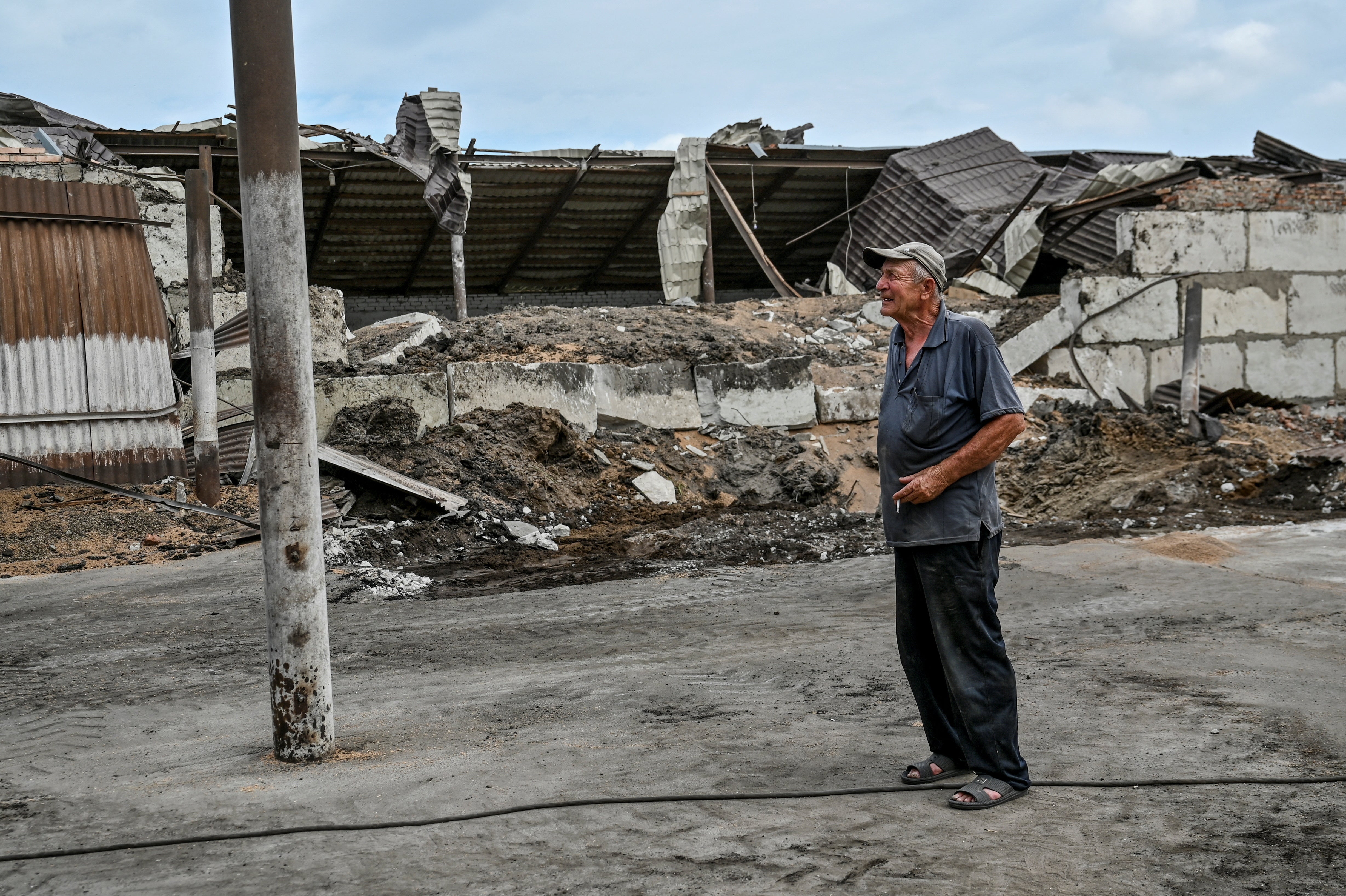 An employee smokes next to a wheat store damaged by a Russian missile strike in the Zaporizhzhia region