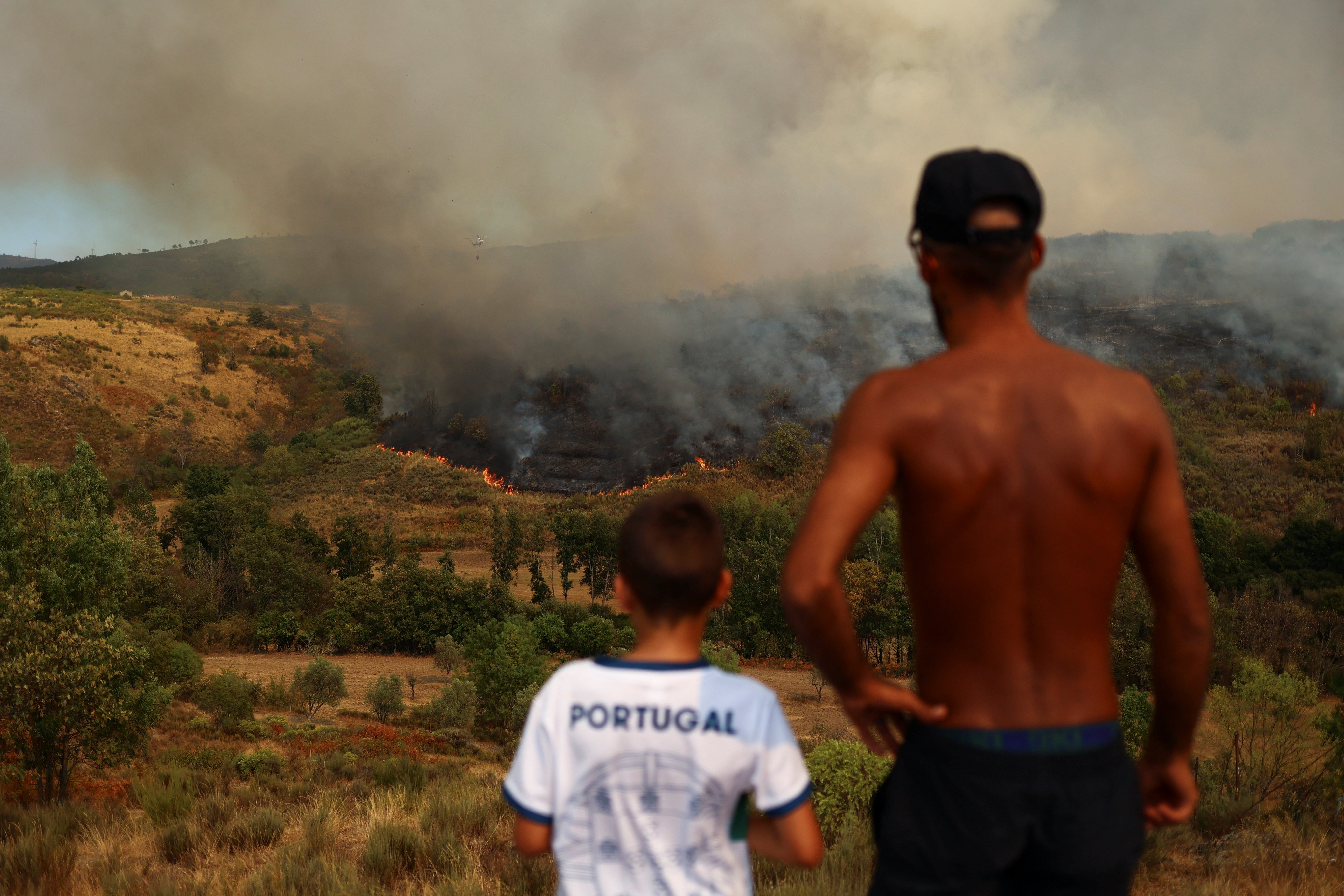 A man and a child watch a wildfire in Carrapichana, Celorico da Beira, Portugal