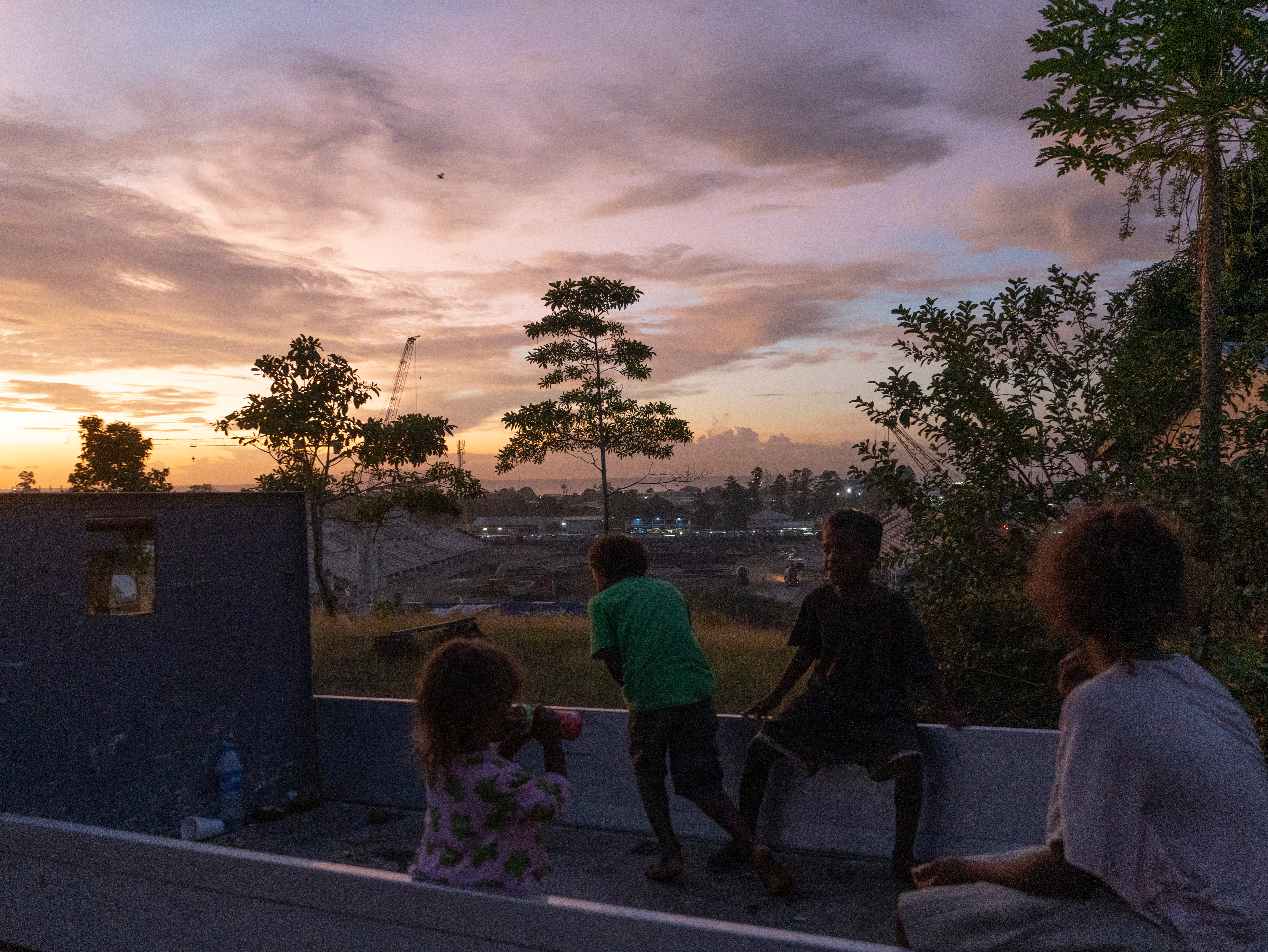 Children watch the sun set over a construction site where China is building a $50m stadium