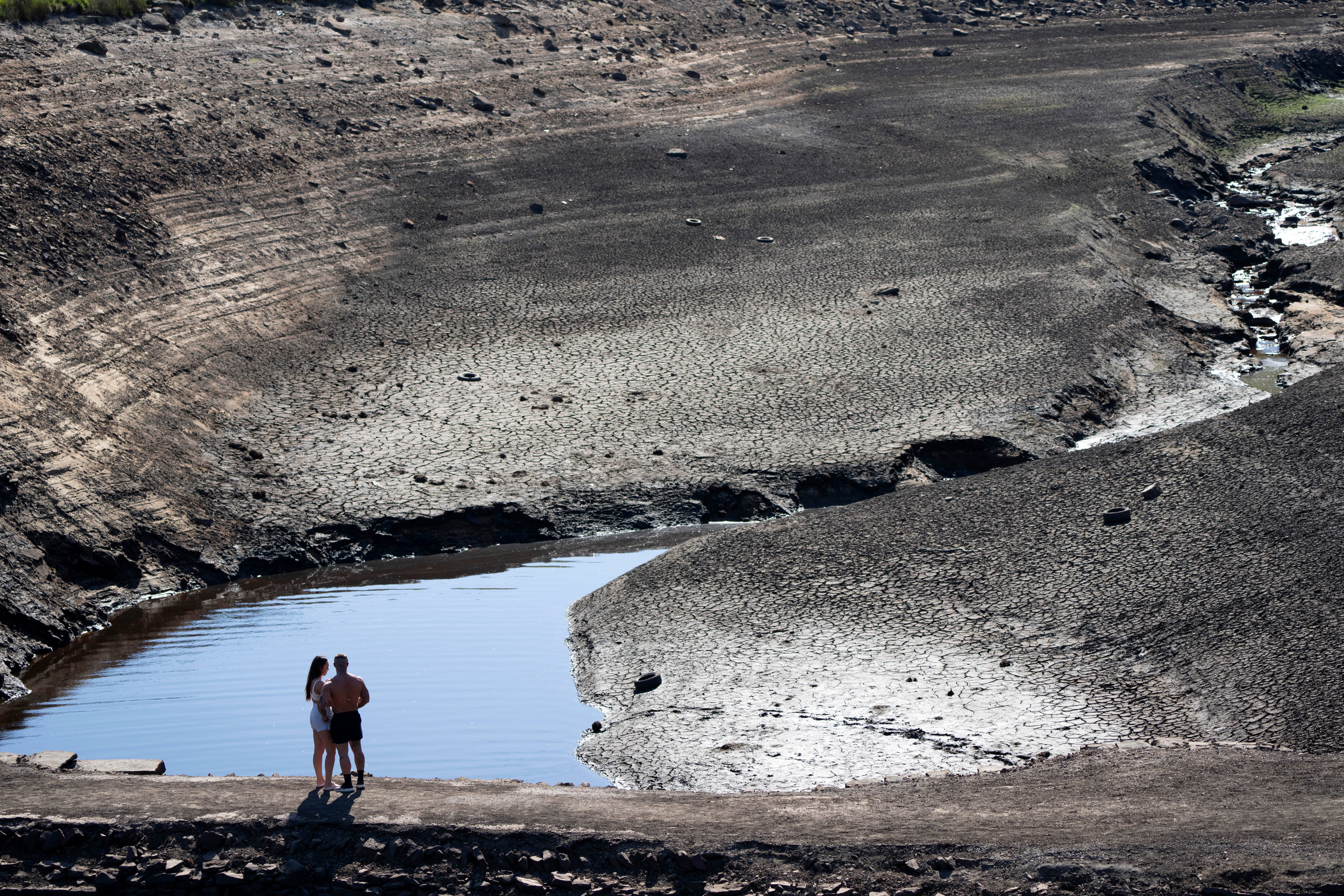 Members of the public stand on what was an ancient packhorse bridge exposed by low water levels at Baitings Reservoir in Yorkshire as record high temperatures are seen in the UK, Ripponden, England