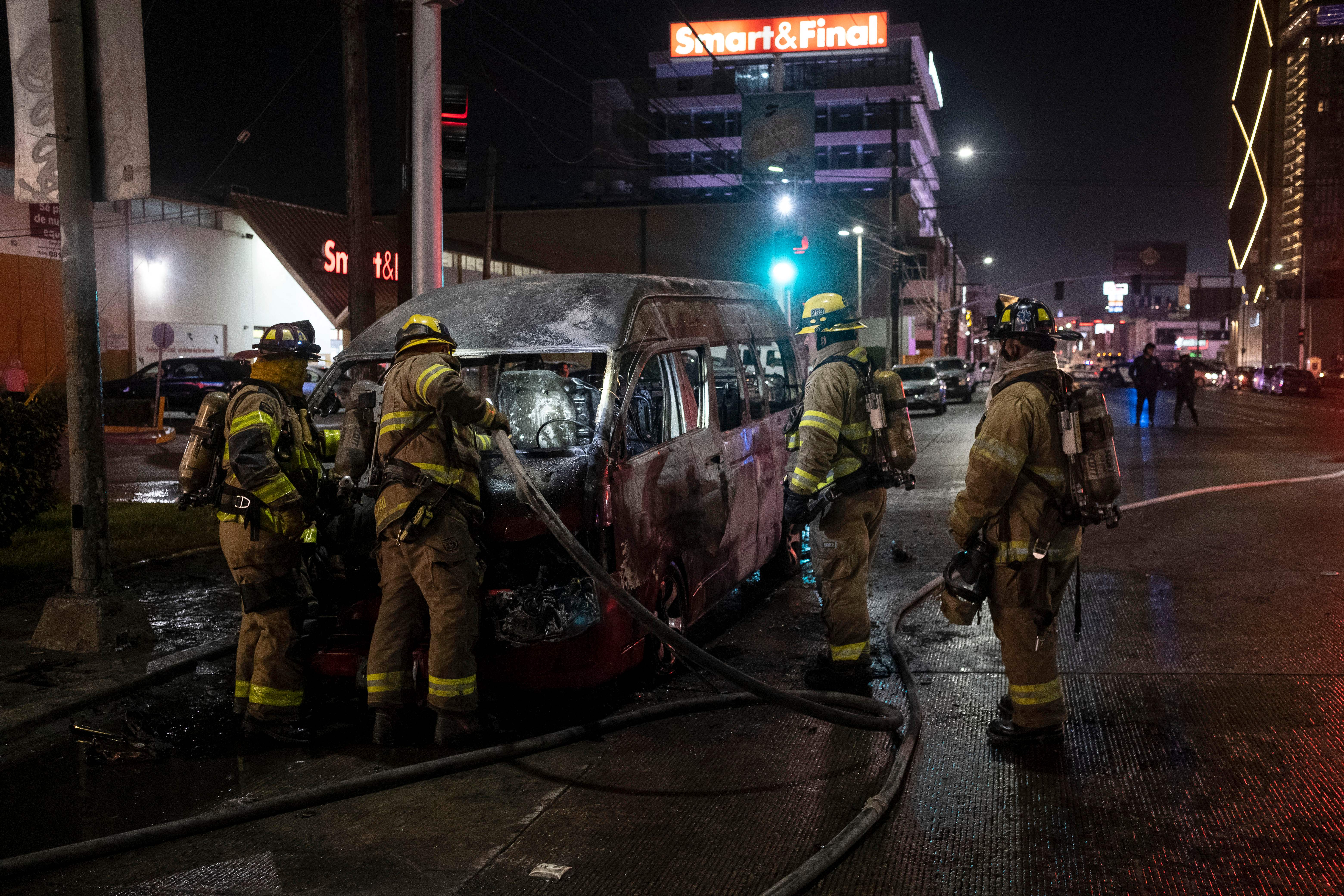 Firefighters work at the scene of a burnt collective transport vehicle after it was set on fire by unidentified individuals in Tijuana, Baja California state, Mexico, on August 12, 2022