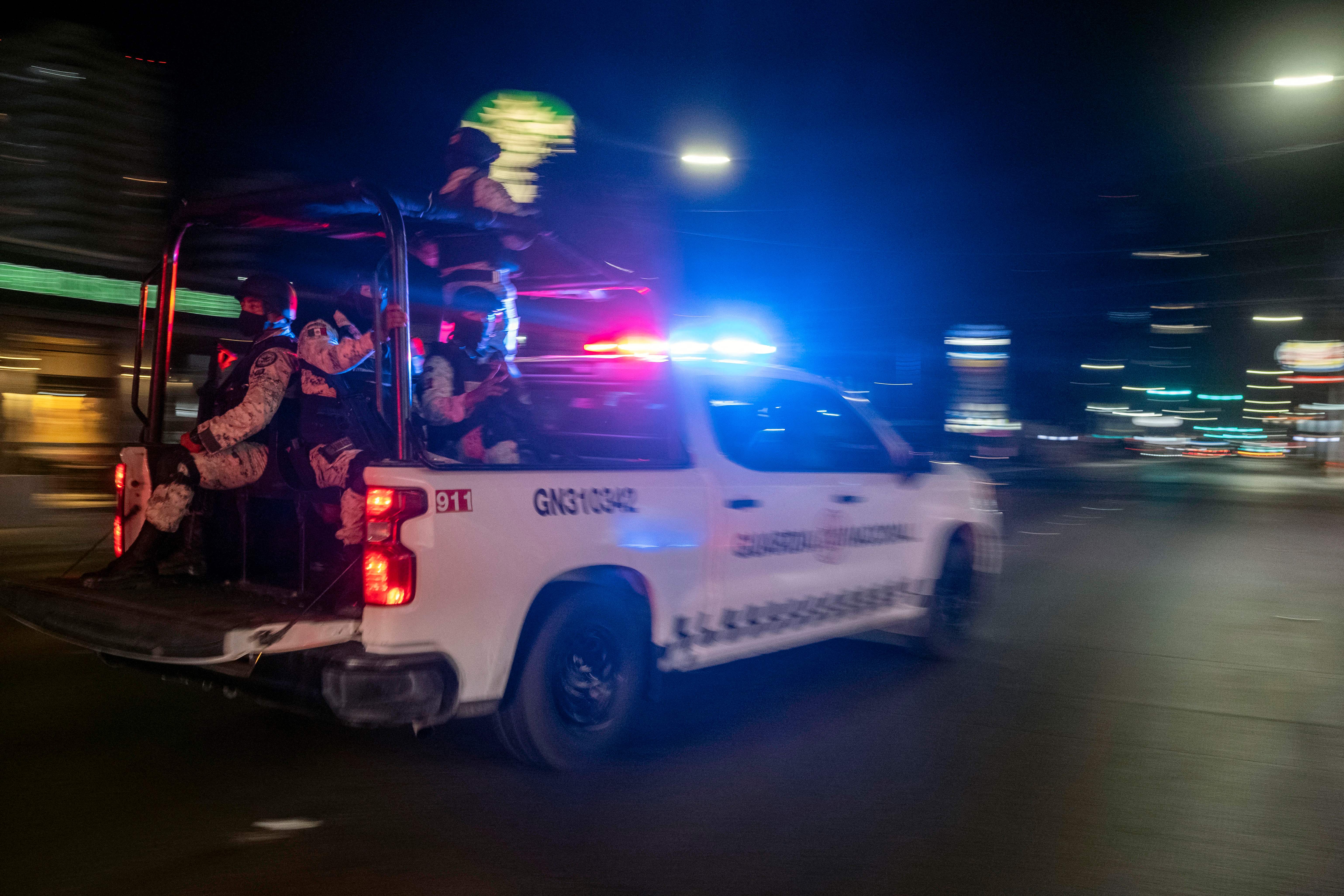 Armed members of the National Guard drive past the site of a burnt collective transport vehicle after it was set on fire by unidentified individuals in Tijuana, Baja California state, Mexico, on August 12, 2022